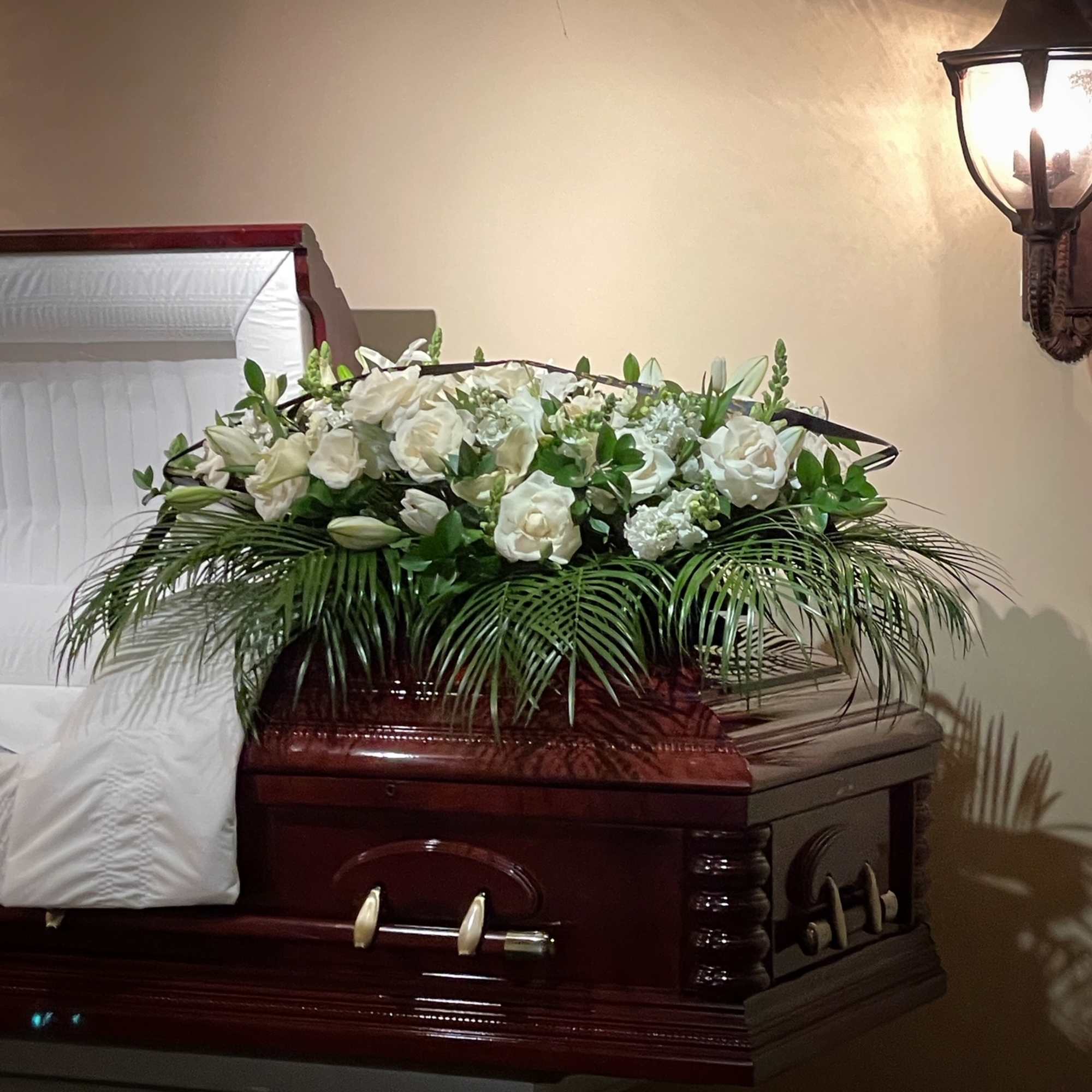 White floral casket spray with greenery on a dark wood casket