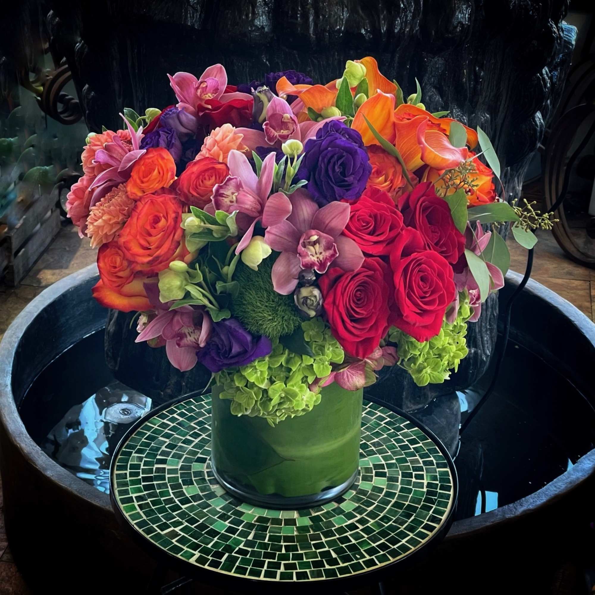 Colorful bouquet of roses, orchids, and calla lilies in a green vase