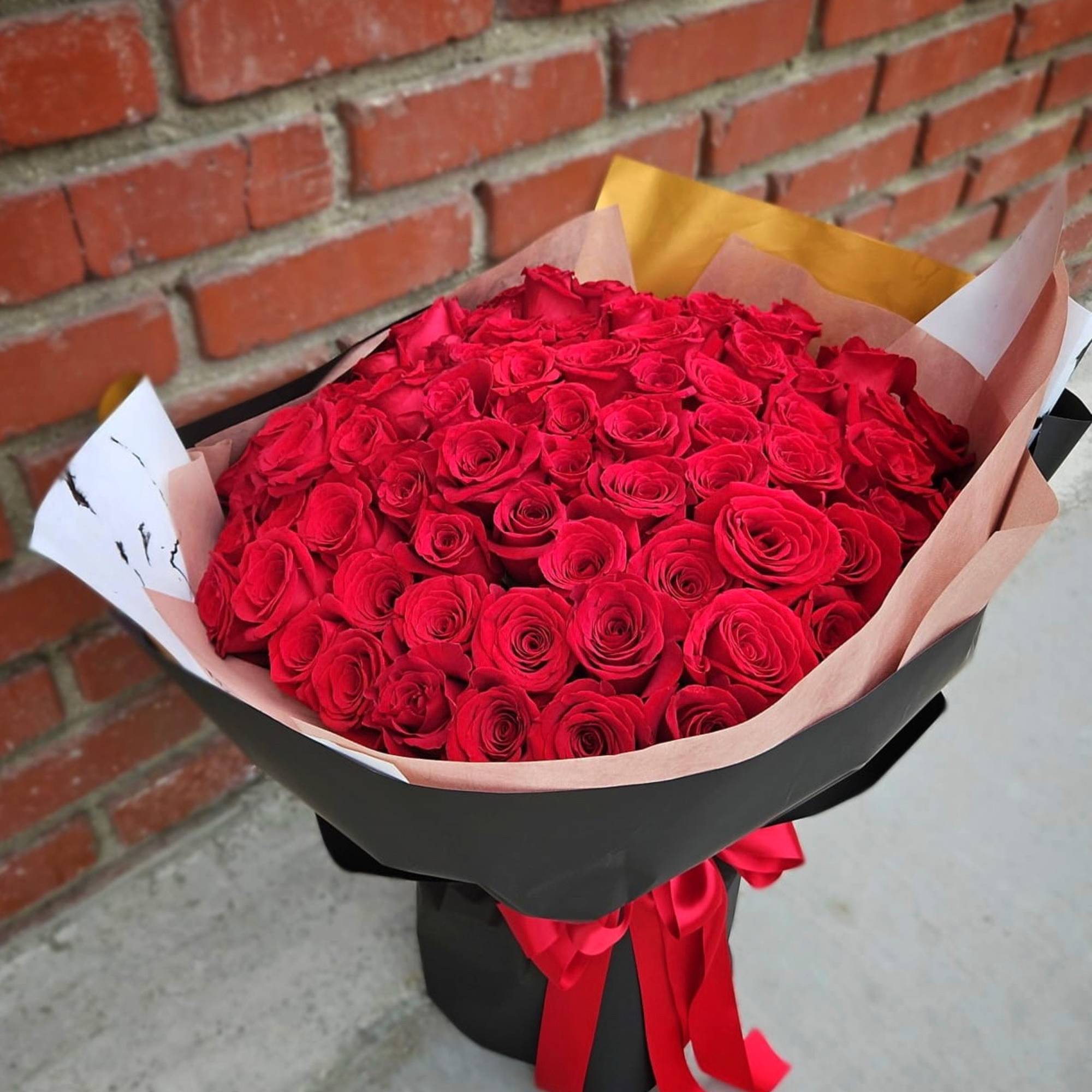 Large bouquet of tightly clustered red roses wrapped in black and blush paper with red ribbons