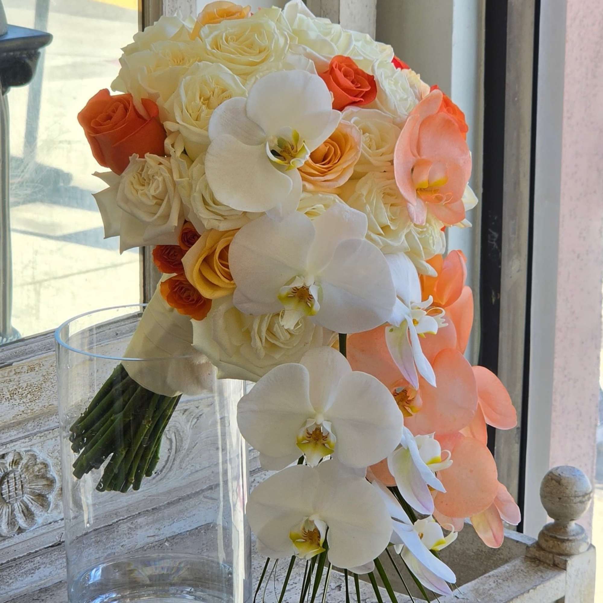 Bouquet of white and peach roses with white orchids in a clear glass vase