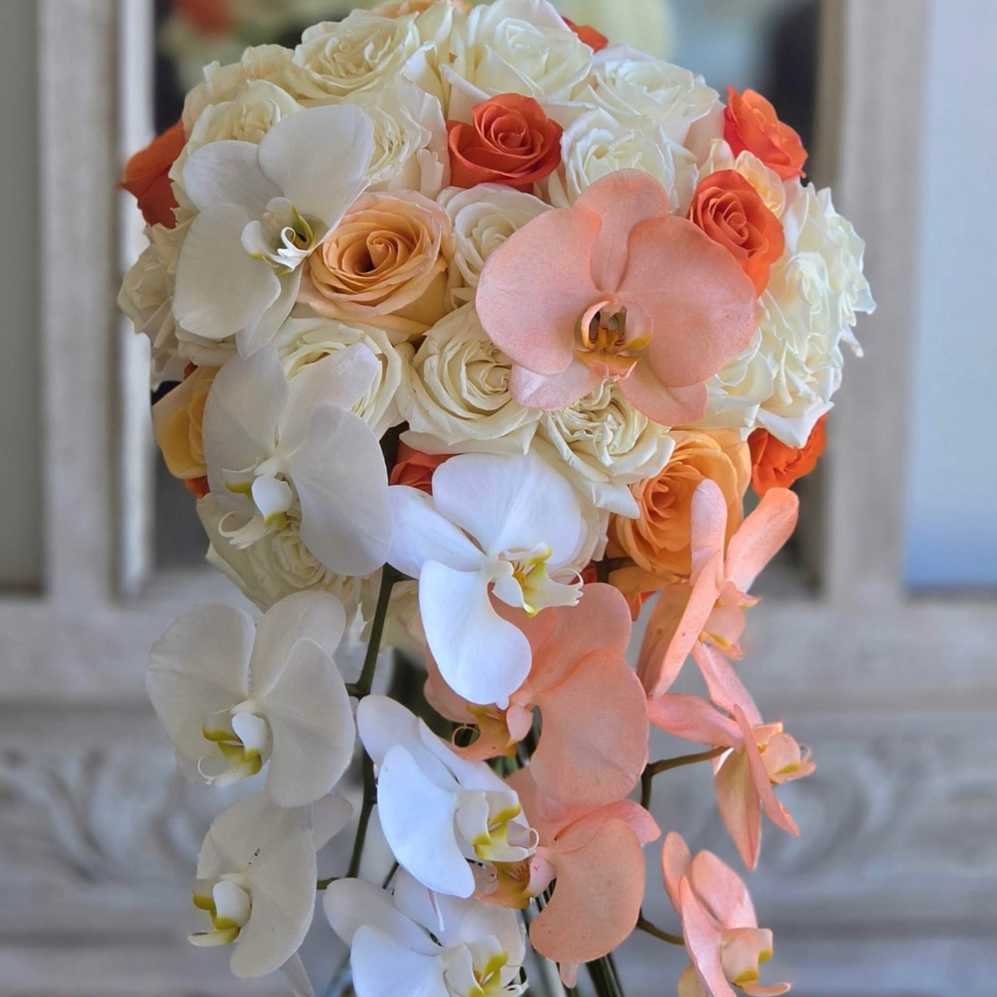 Bouquet of white and peach roses with cascading orchids in a glass vase