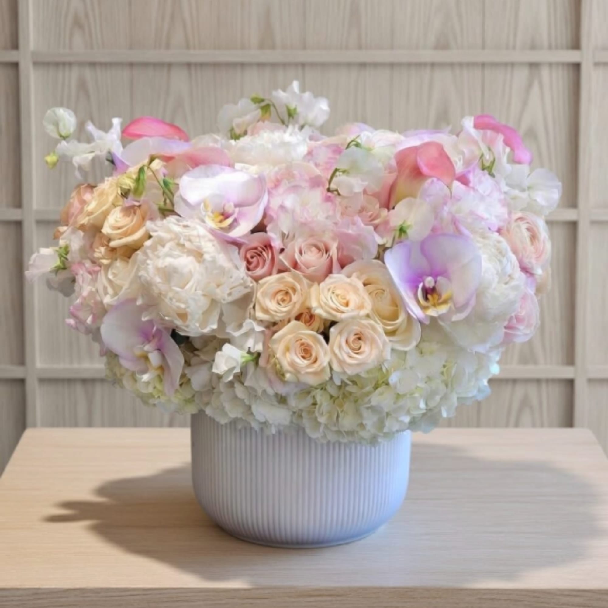 Pastel bouquet of roses, hydrangeas, and calla lilies in a ribbed white vase.