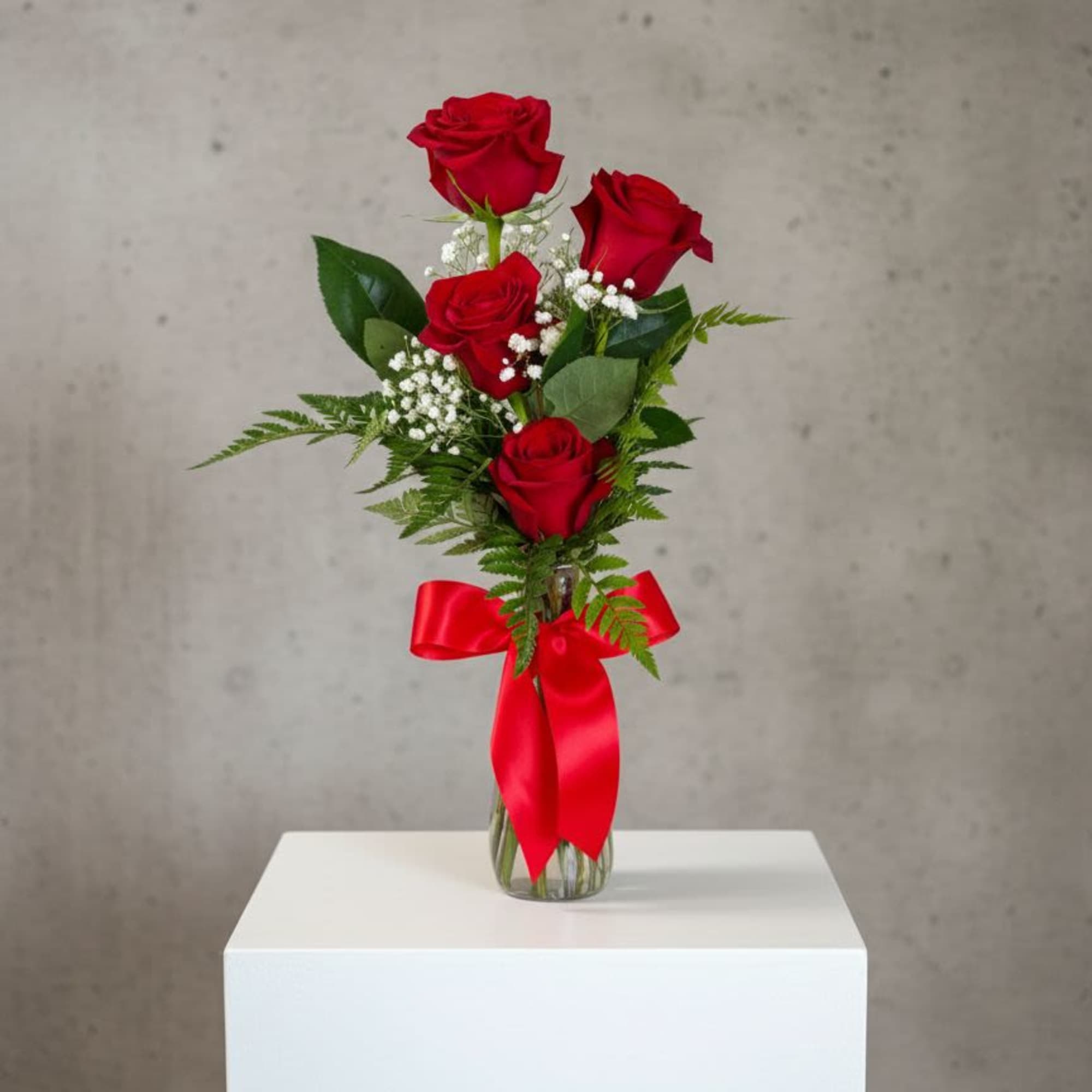 Red roses in a clear glass vase with a red ribbon