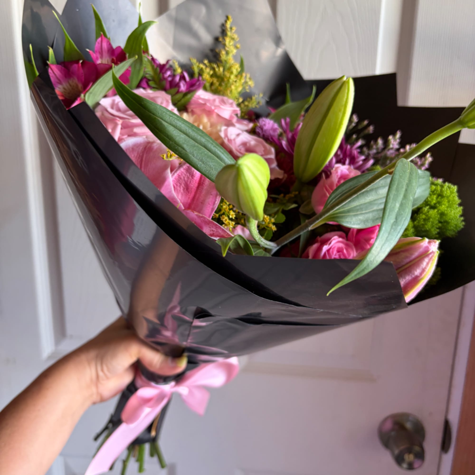 Handheld bouquet of pink lilies and roses wrapped in black paper