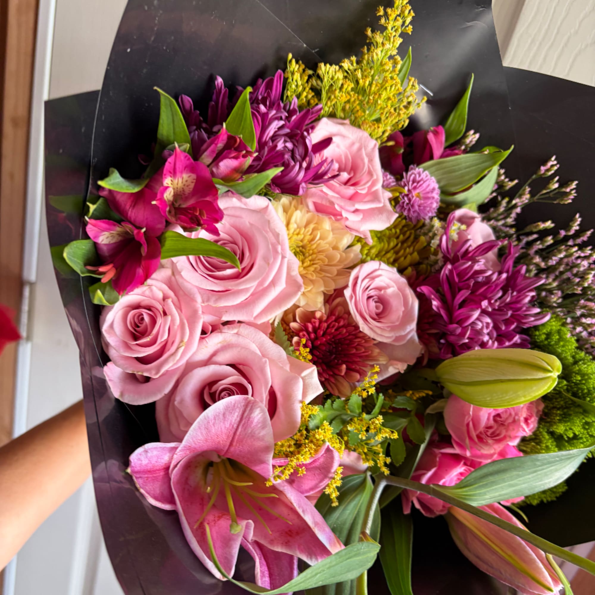 Bouquet of pink roses, lilies, and purple flowers wrapped in black paper