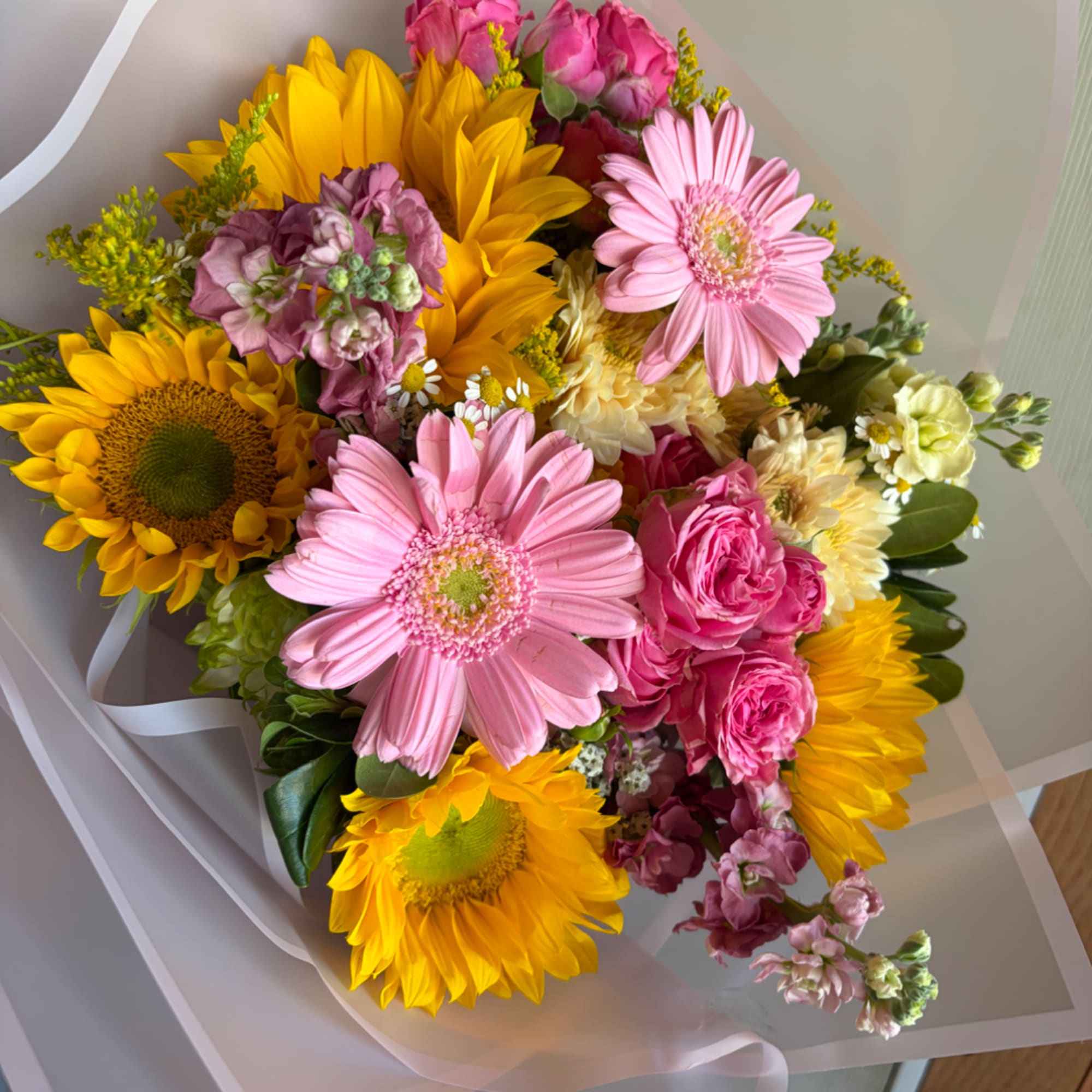 Bouquet of pink gerbera daisies, yellow sunflowers, and roses wrapped in white paper
