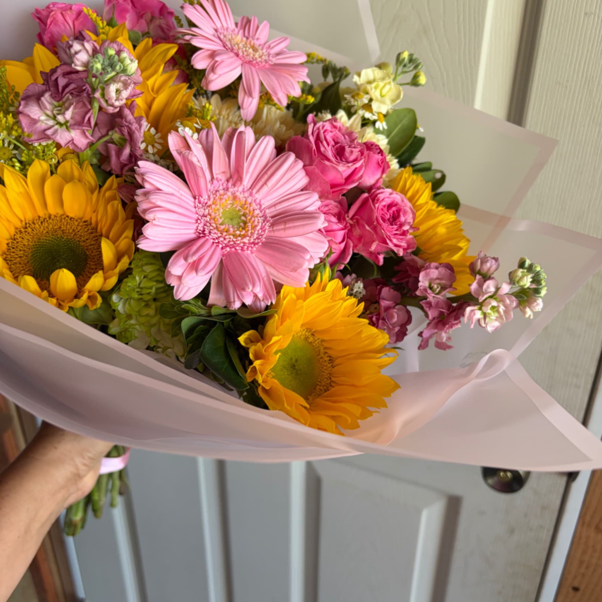 Handheld bouquet of pink and yellow flowers wrapped in pale pink paper