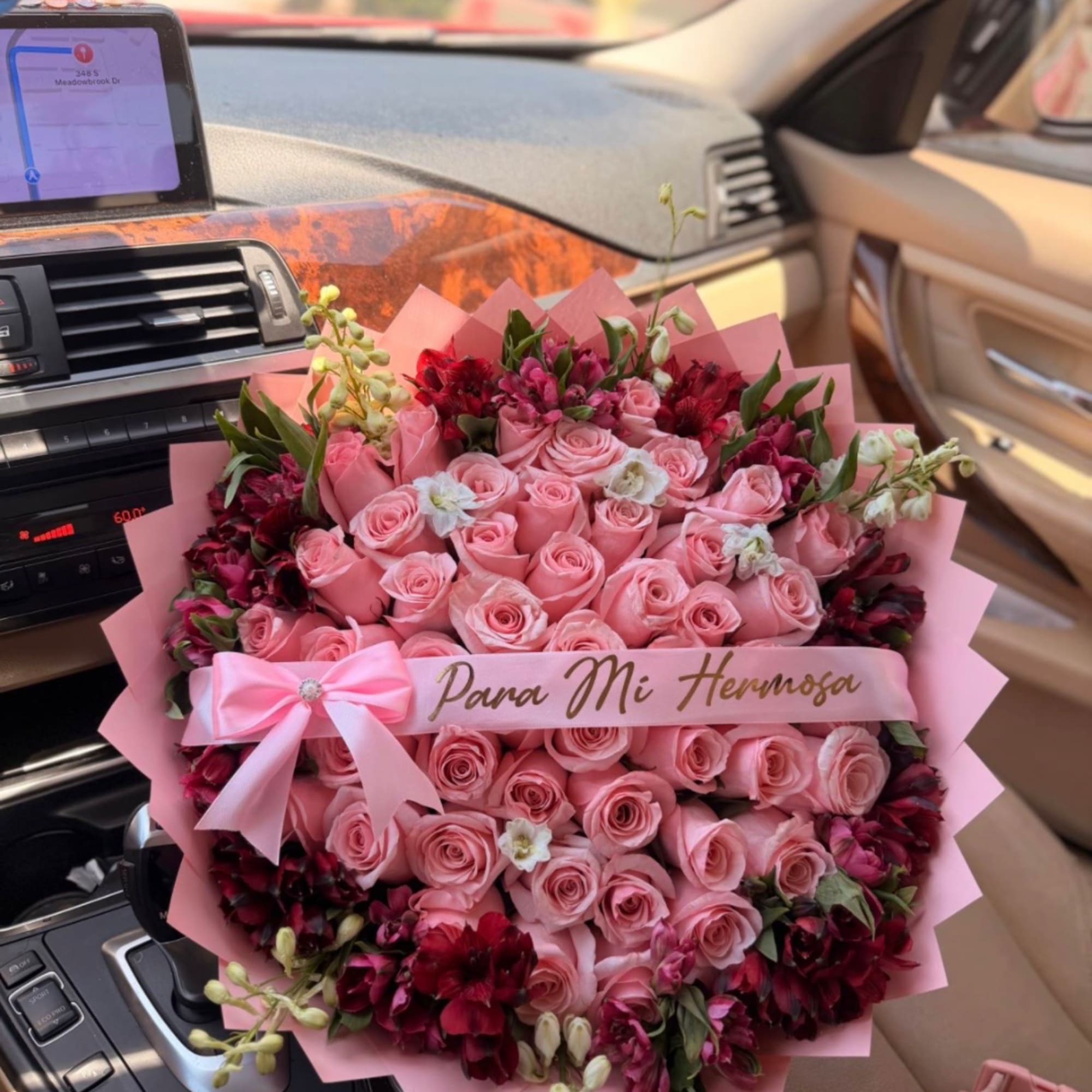 Pink rose bouquet with dark red accent flowers and a ribbon in a car