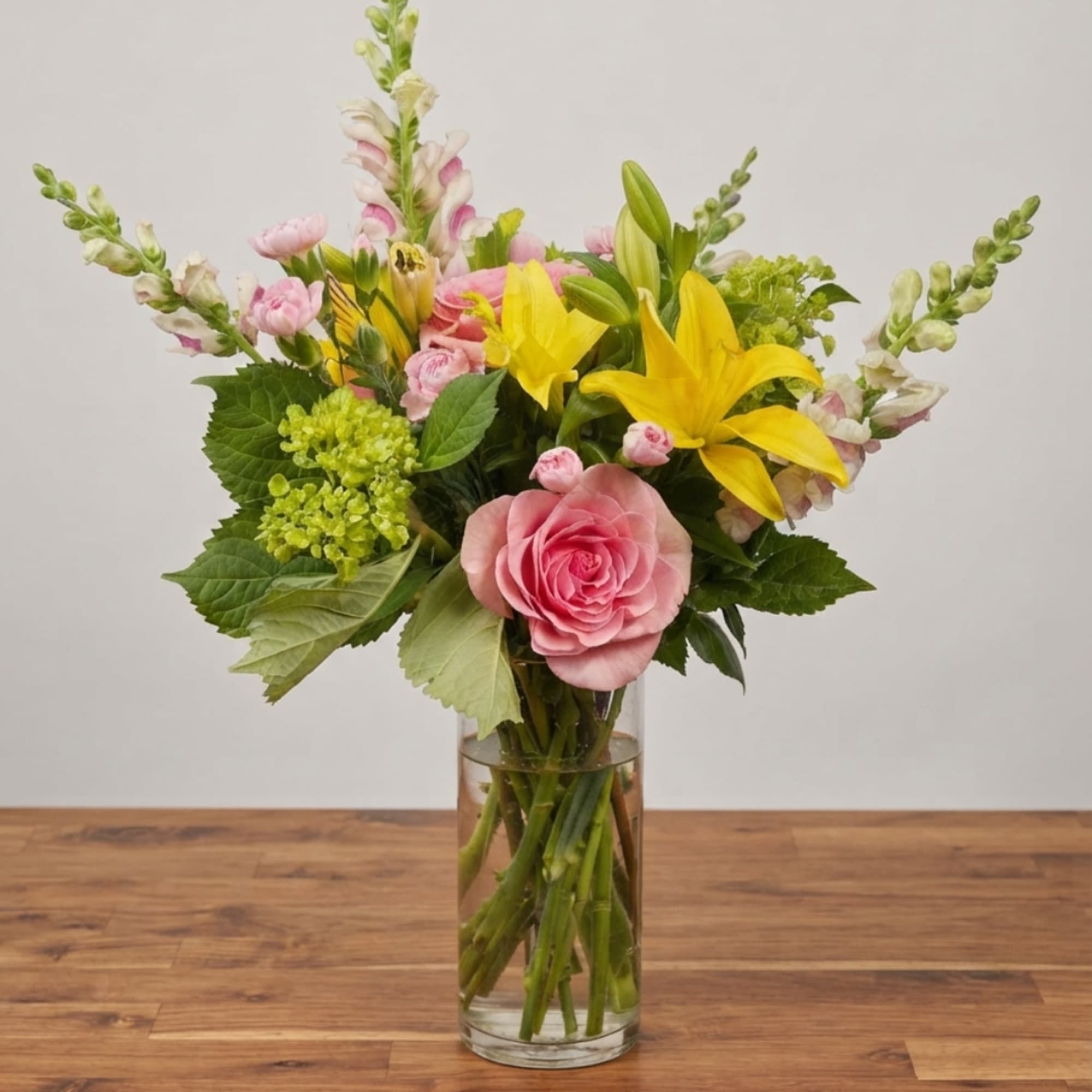 Pink roses and yellow lilies arranged in a clear glass vase