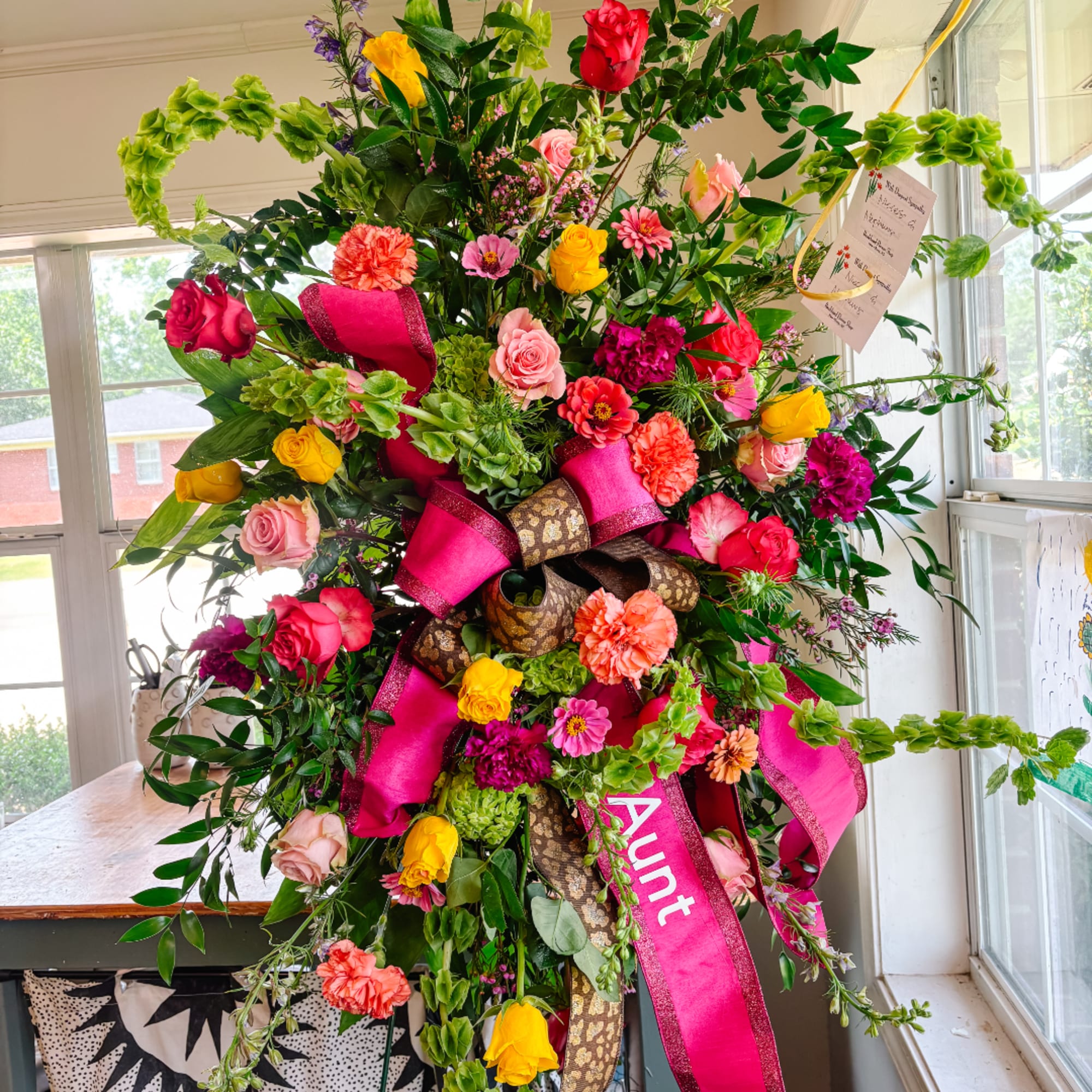 Large colorful floral standing arrangement with pink ribbons and an Aunt sash