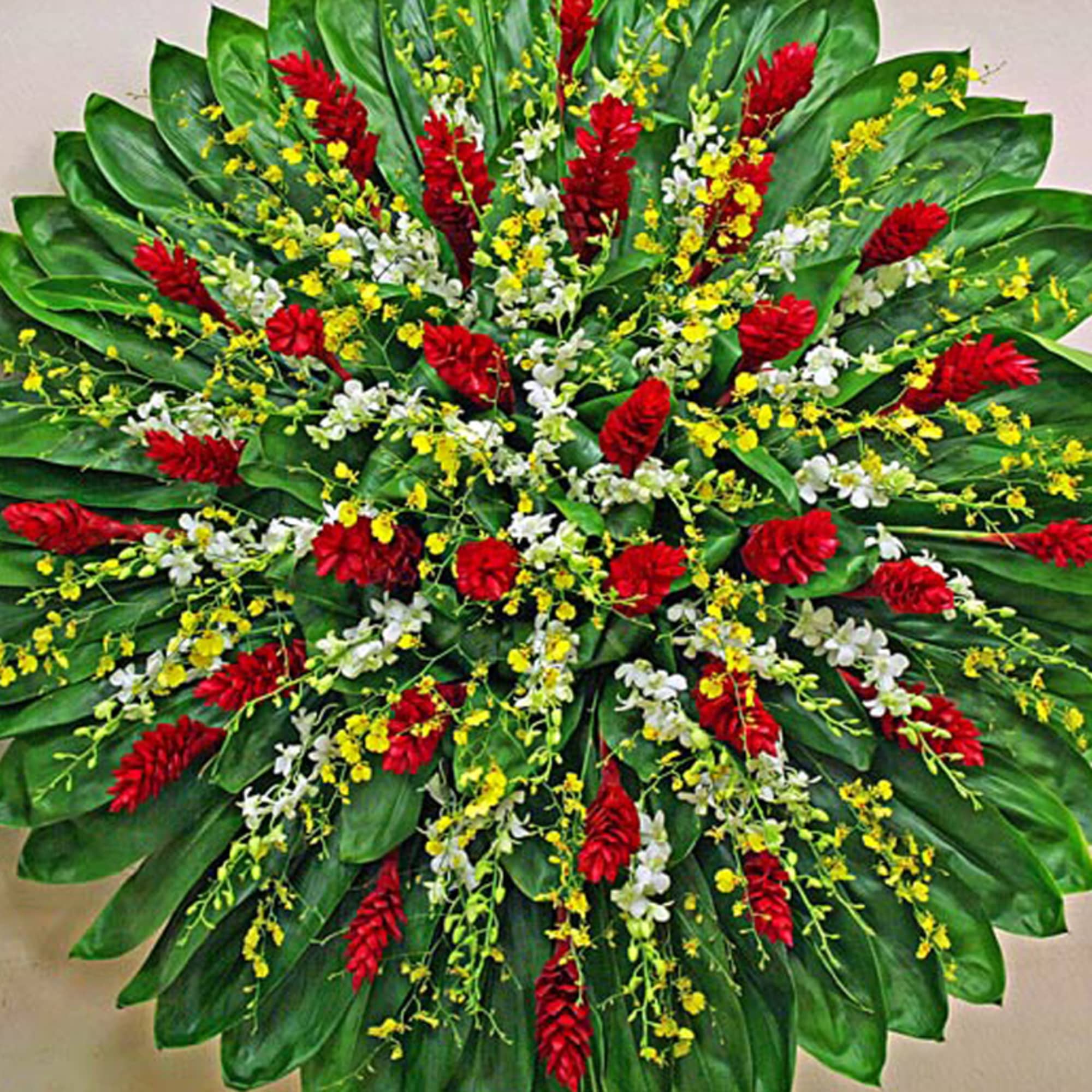 Large round tropical arrangement with red flowers and yellow and white orchids over layered green leaves