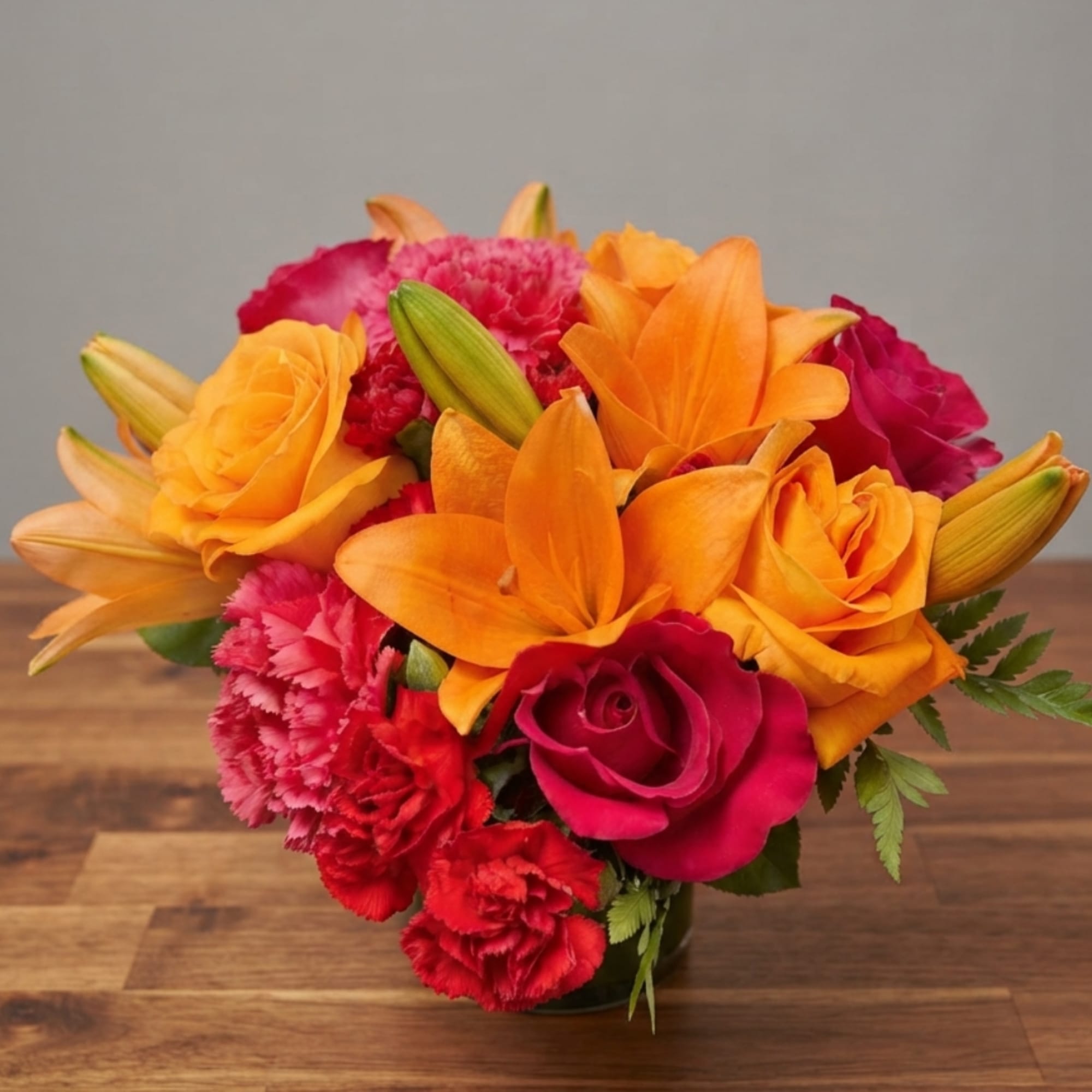 Orange lilies and pink roses in a low vase with red carnations