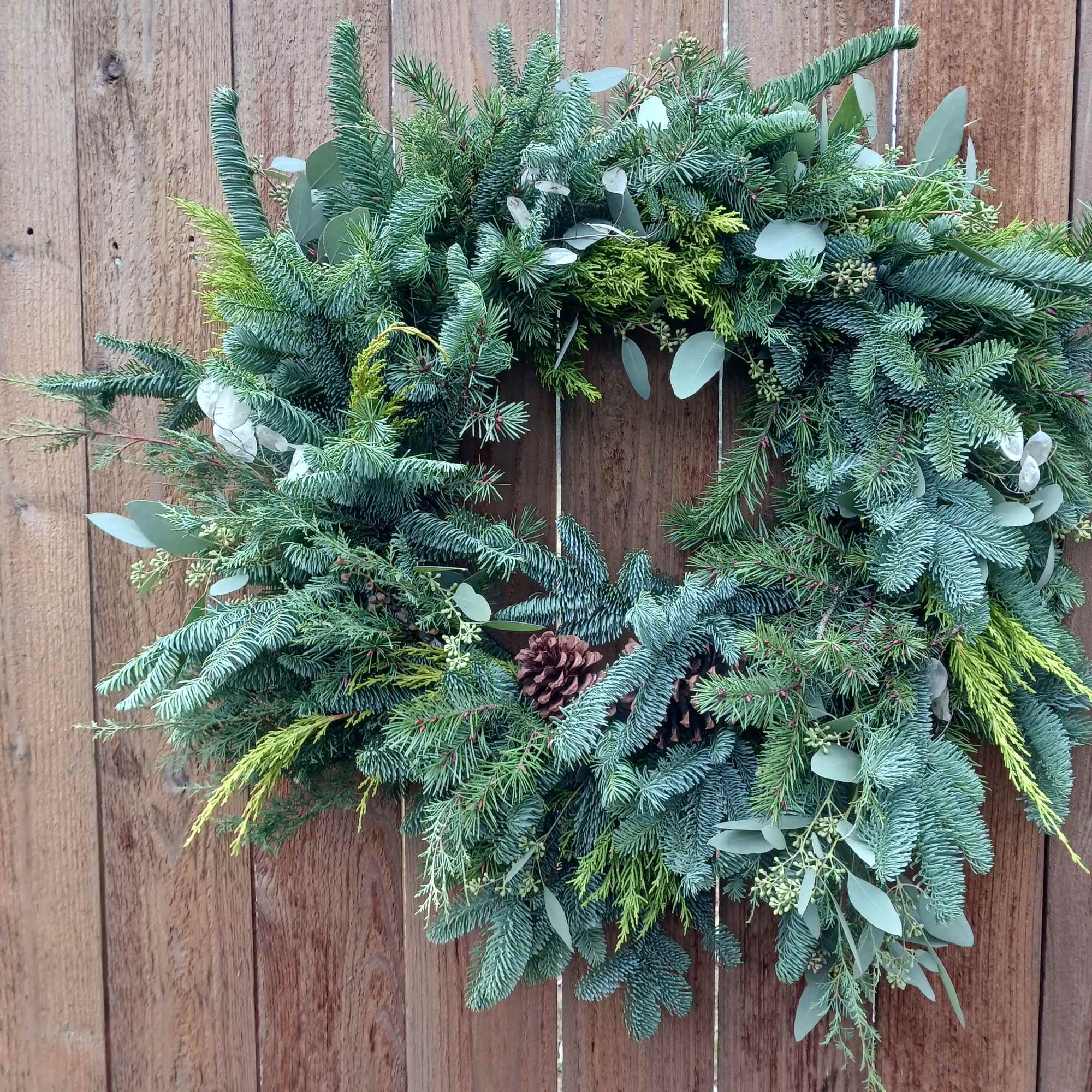 Evergreen wreath with pinecones and mixed foliage hanging on a wooden fence