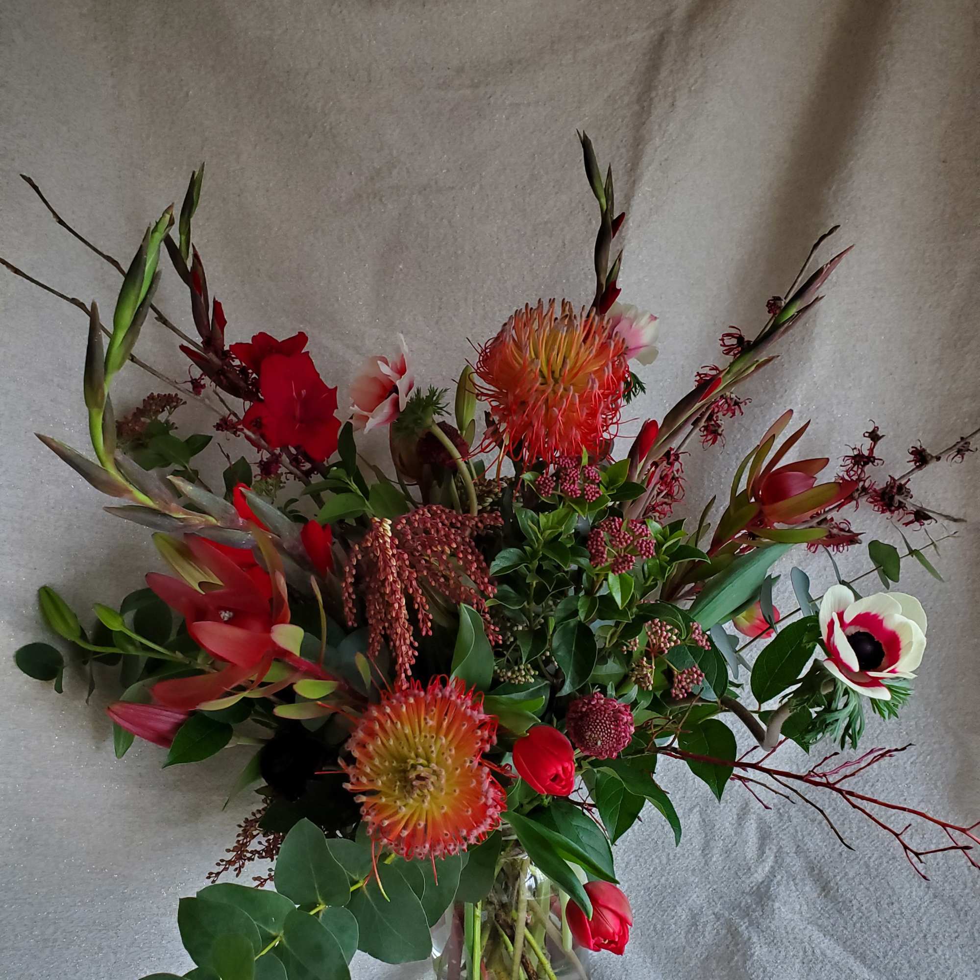 Tall arrangement of red and orange blooms with tulips and anemone in a clear glass vase