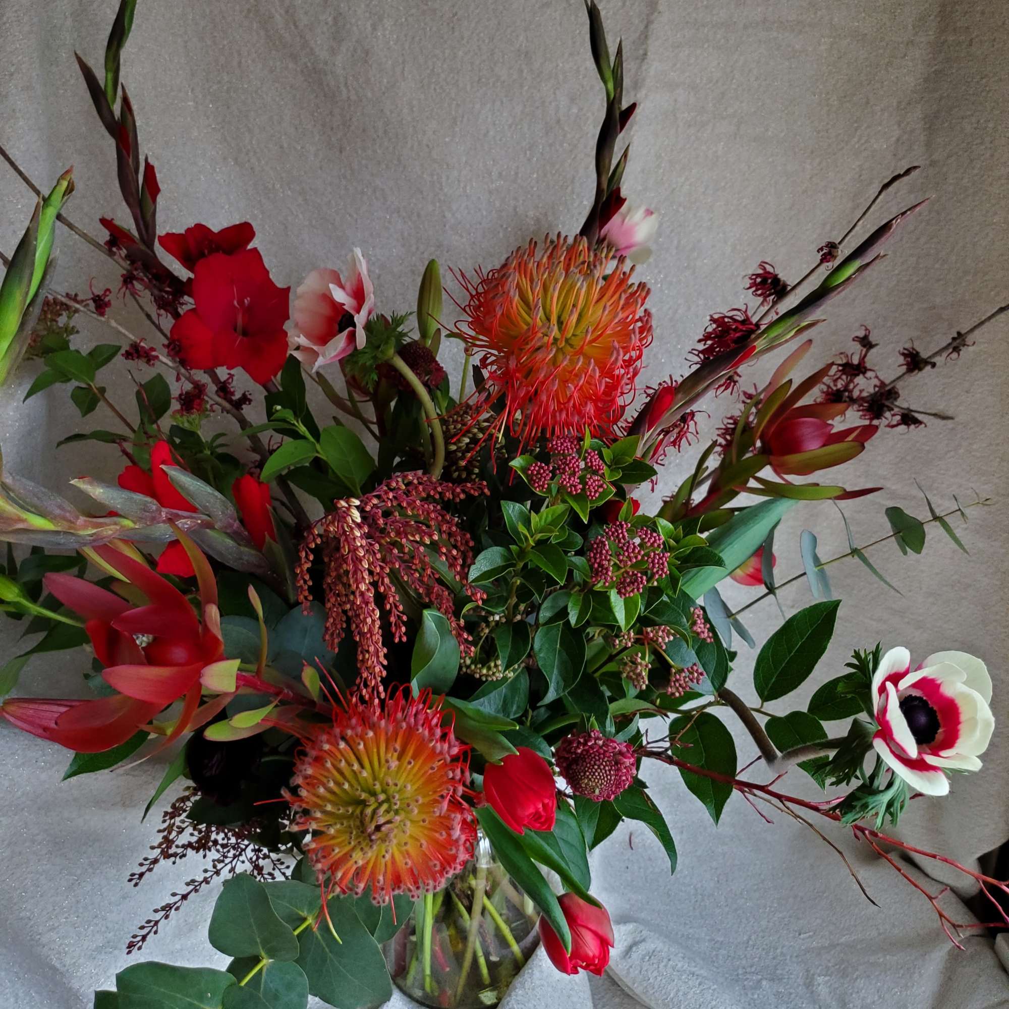 Tall red and white floral arrangement with pincushion protea in a clear glass vase.
