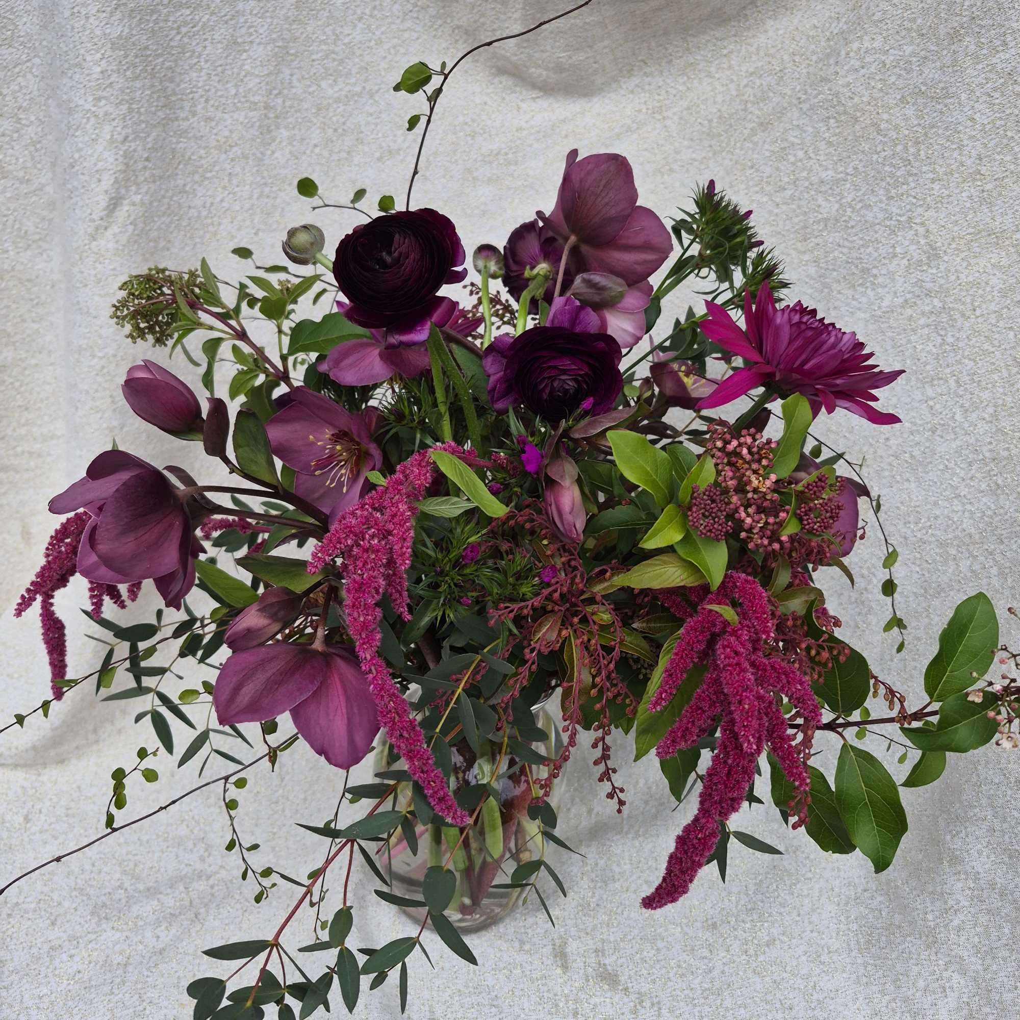 Asymmetrical bouquet of dark purple and magenta flowers in a clear glass vase