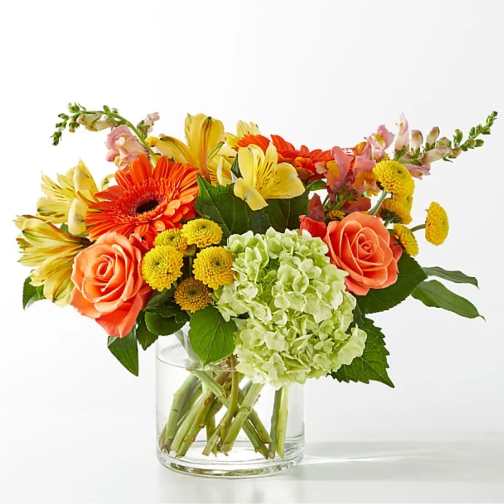 Mixed bouquet of orange roses, yellow lilies, and green hydrangea in a clear glass vase