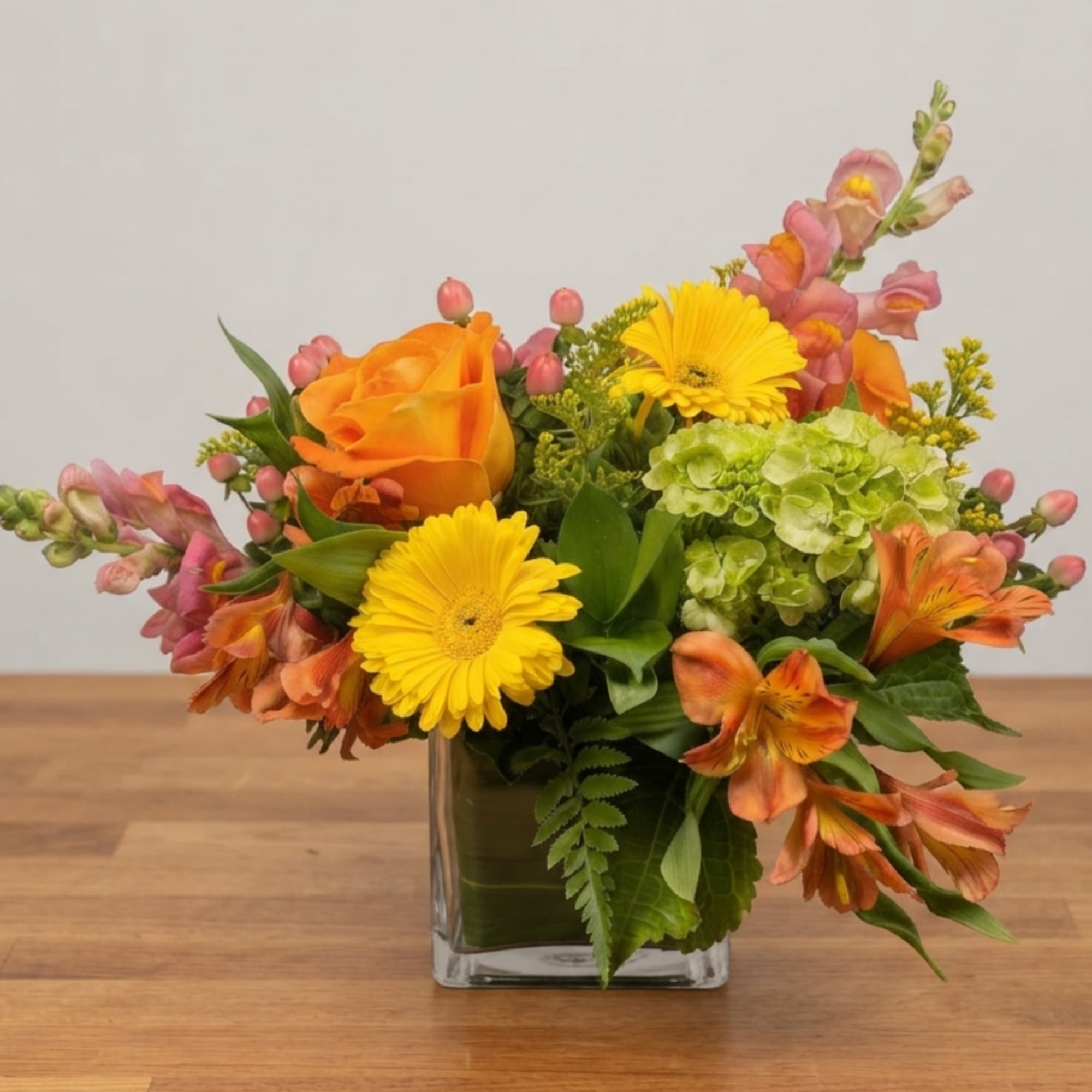 Orange roses and yellow daisies in a clear glass vase
