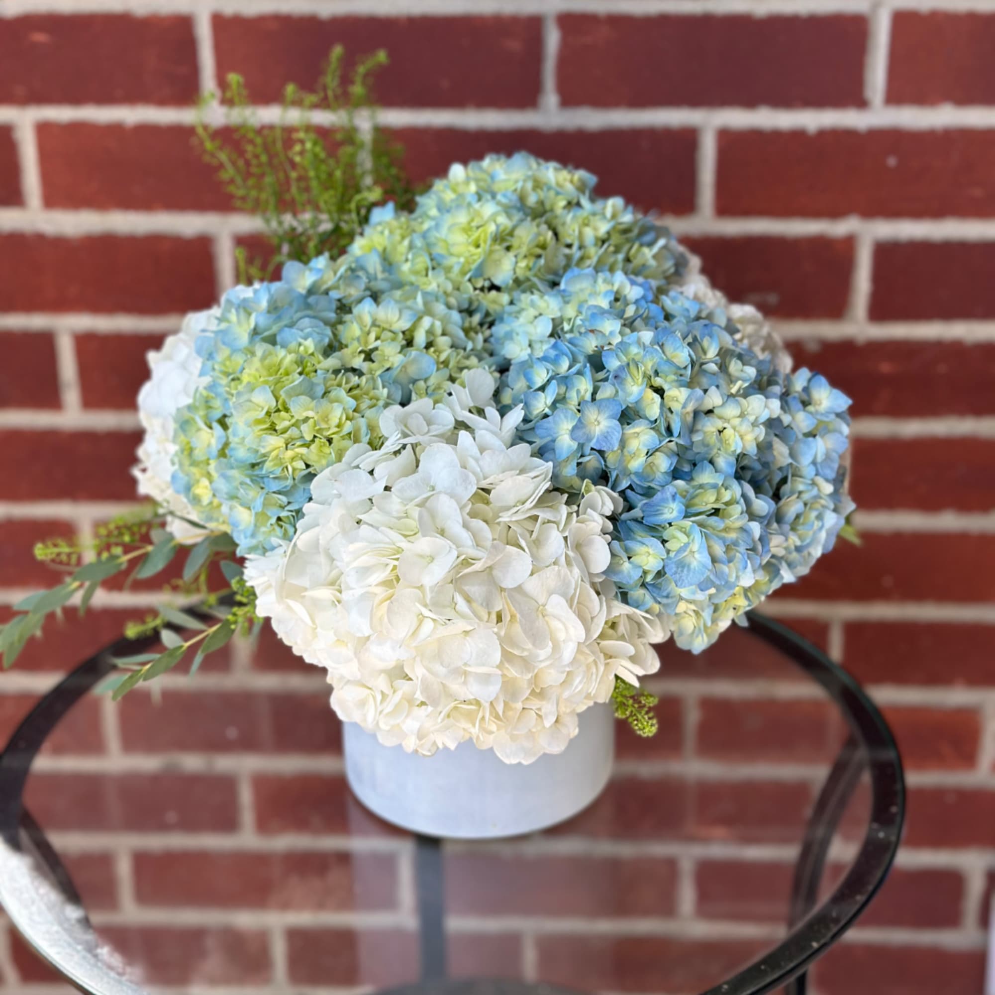 Blue and white hydrangea arrangement in a white container