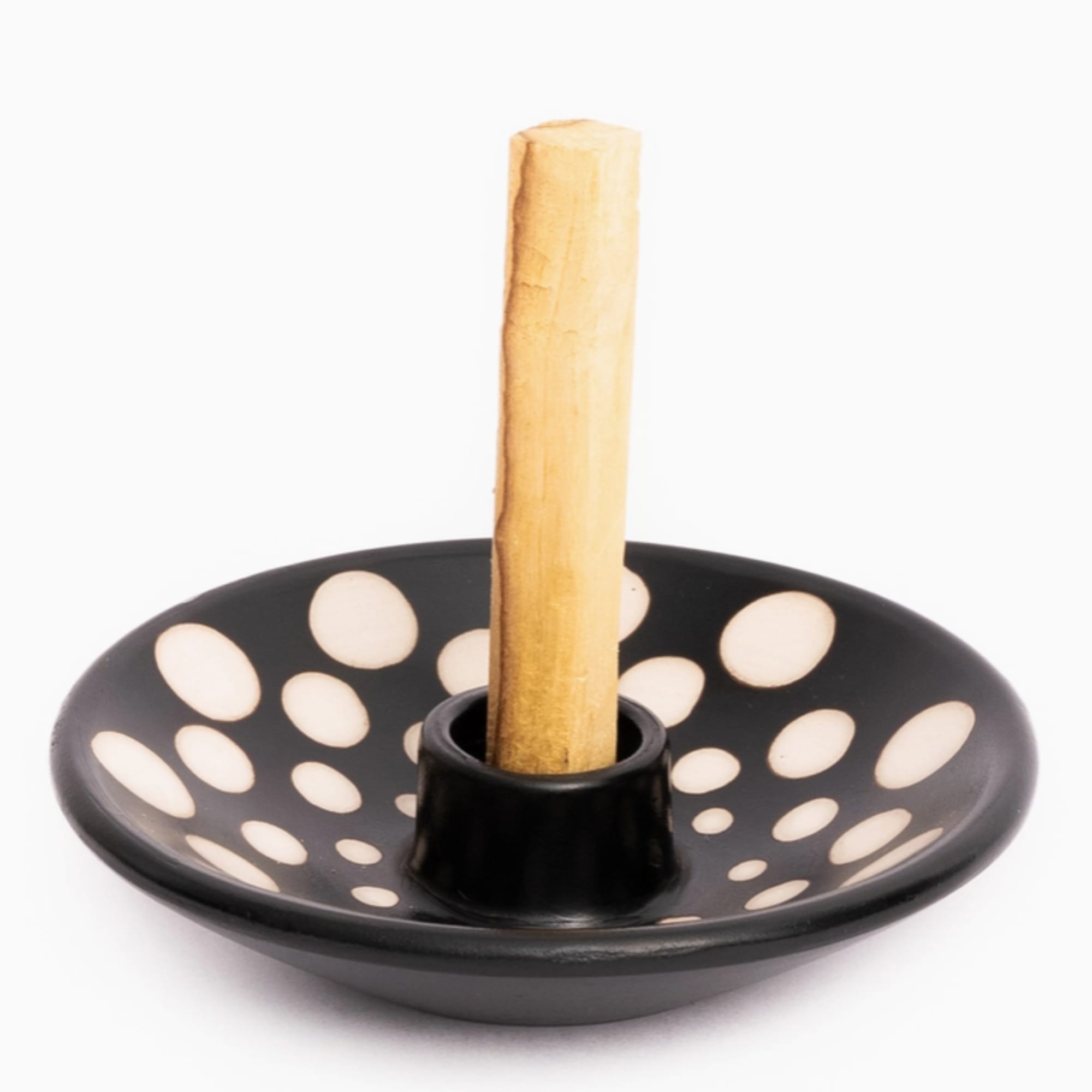 Black ceramic incense holder with white dots and a wooden stick