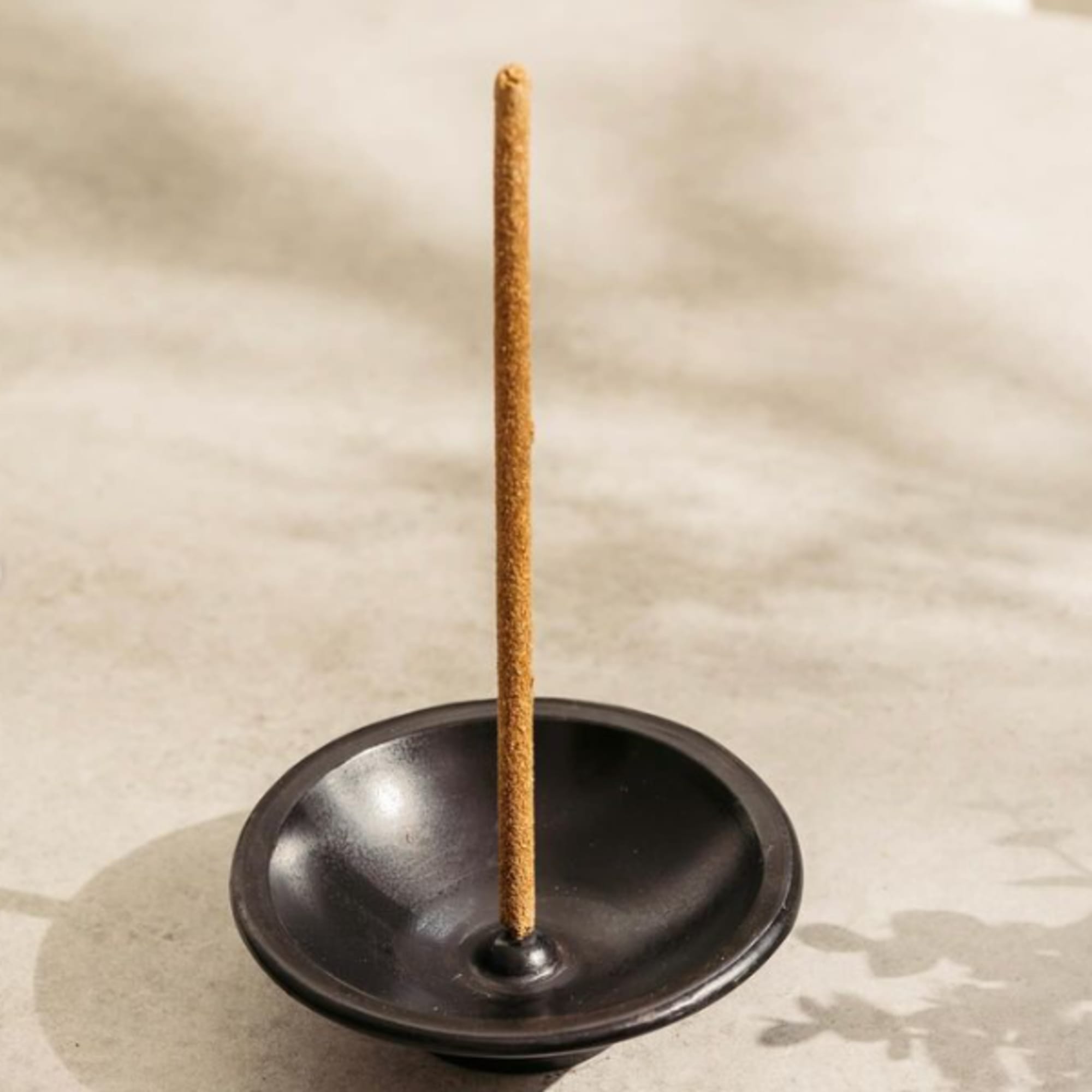 A single incense stick stands in a small black holder.