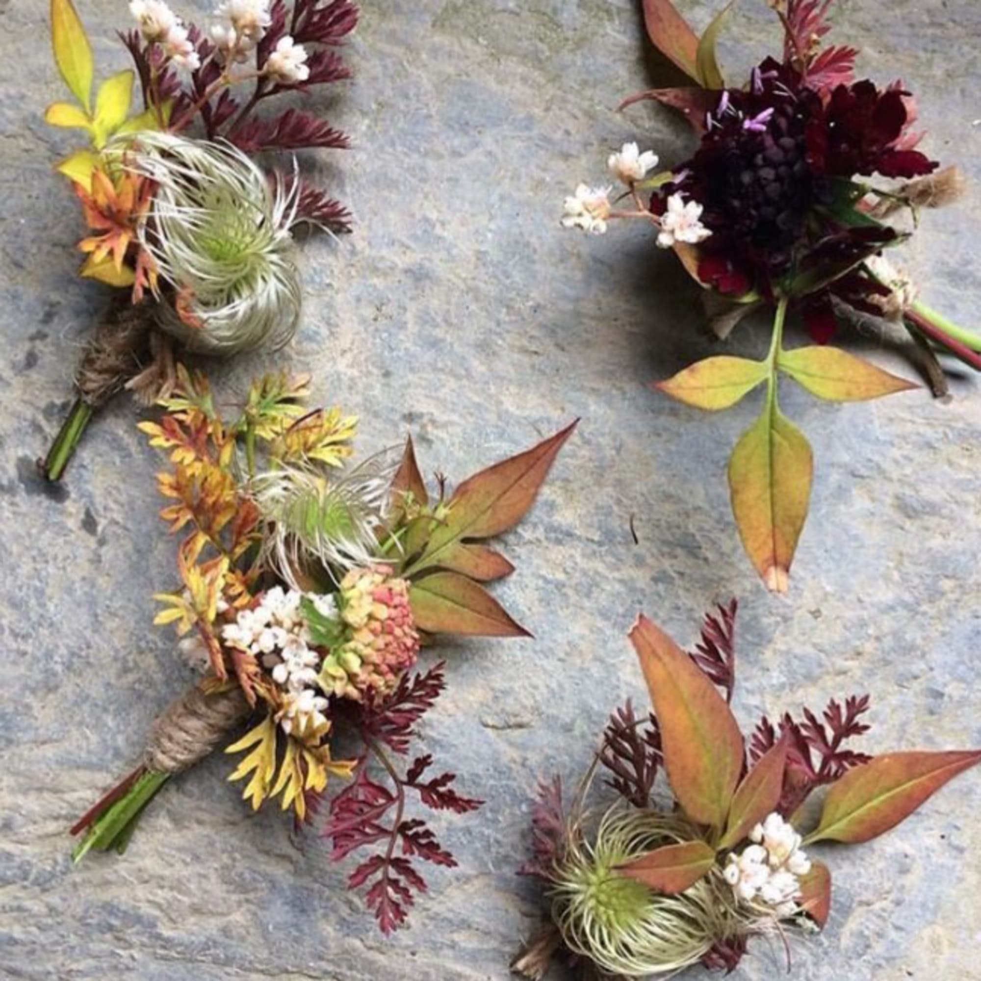 Four small floral boutonnieres with autumn-colored leaves and white accents