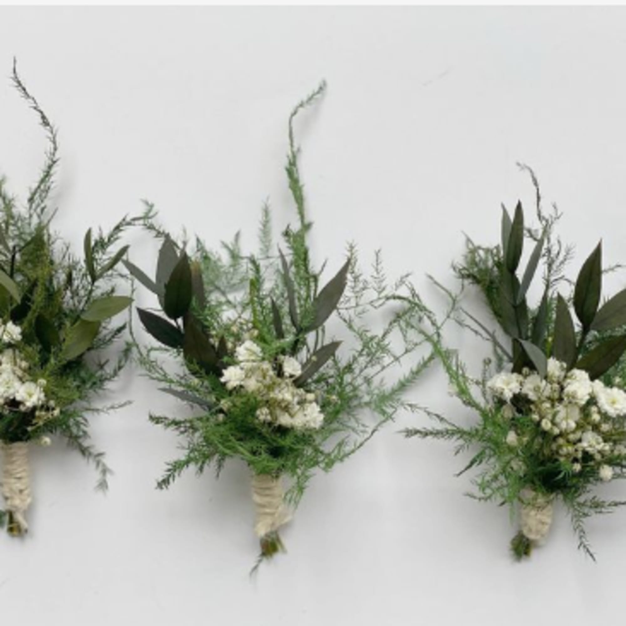 Three small white floral bouquets with greenery on a white background