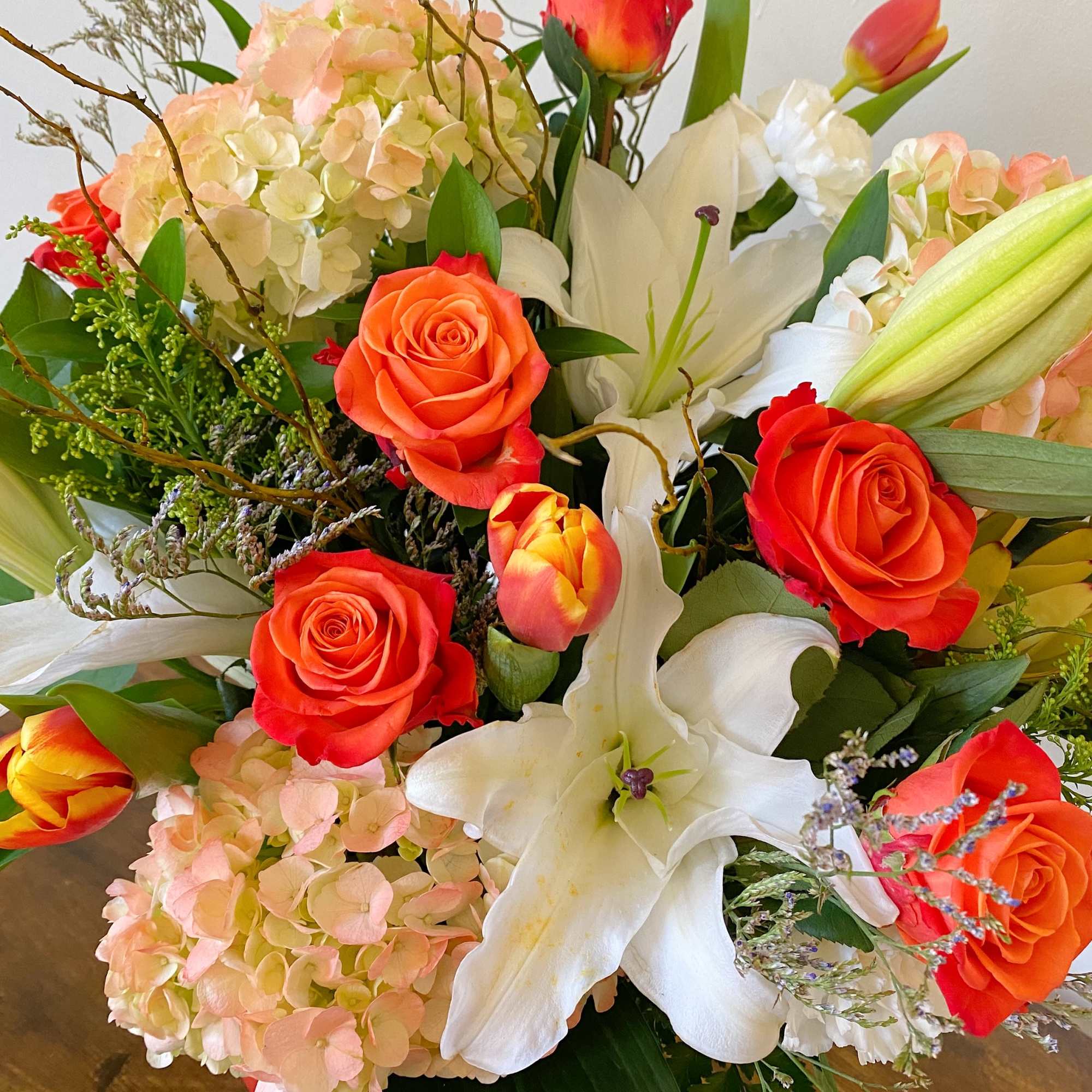 Arrangement of orange roses, tulips, pale hydrangeas, and white lilies in a mixed bouquet