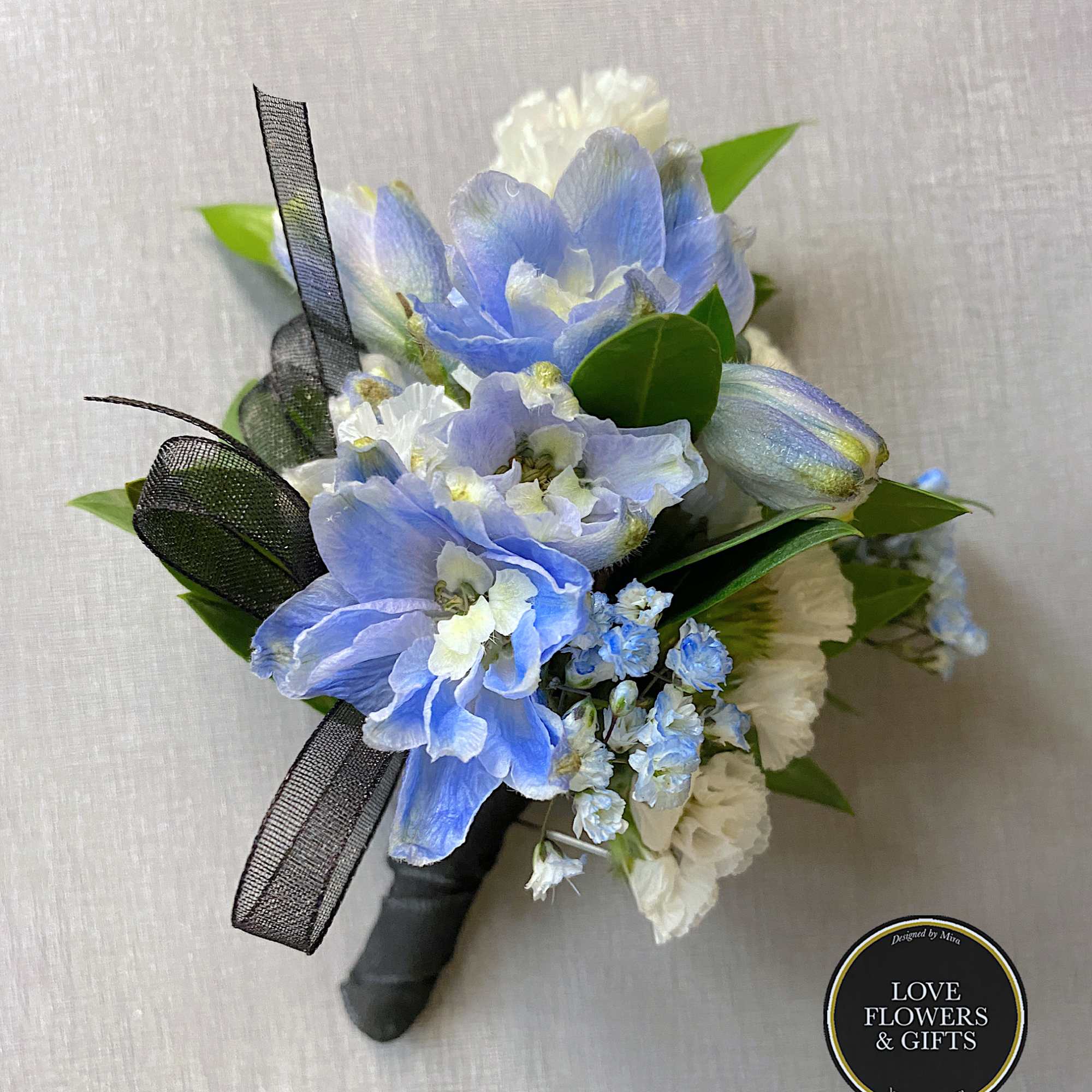 Blue and white boutonniere with delphinium and carnations tied with black ribbon