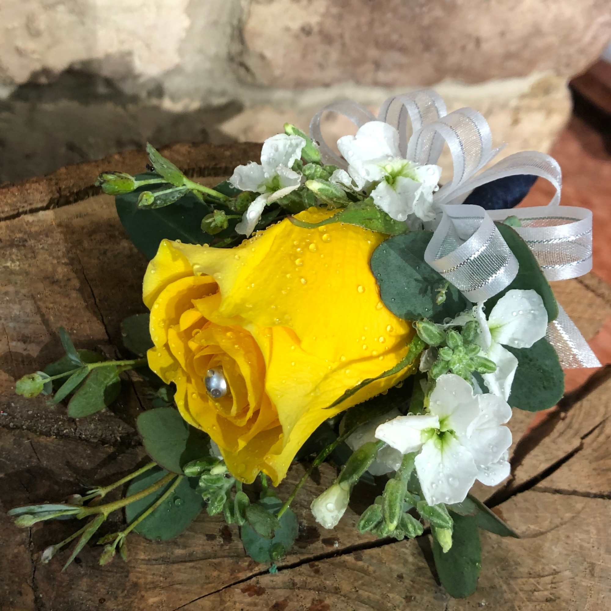 Yellow rose corsage with white accent flowers and silver ribbon on rustic wood