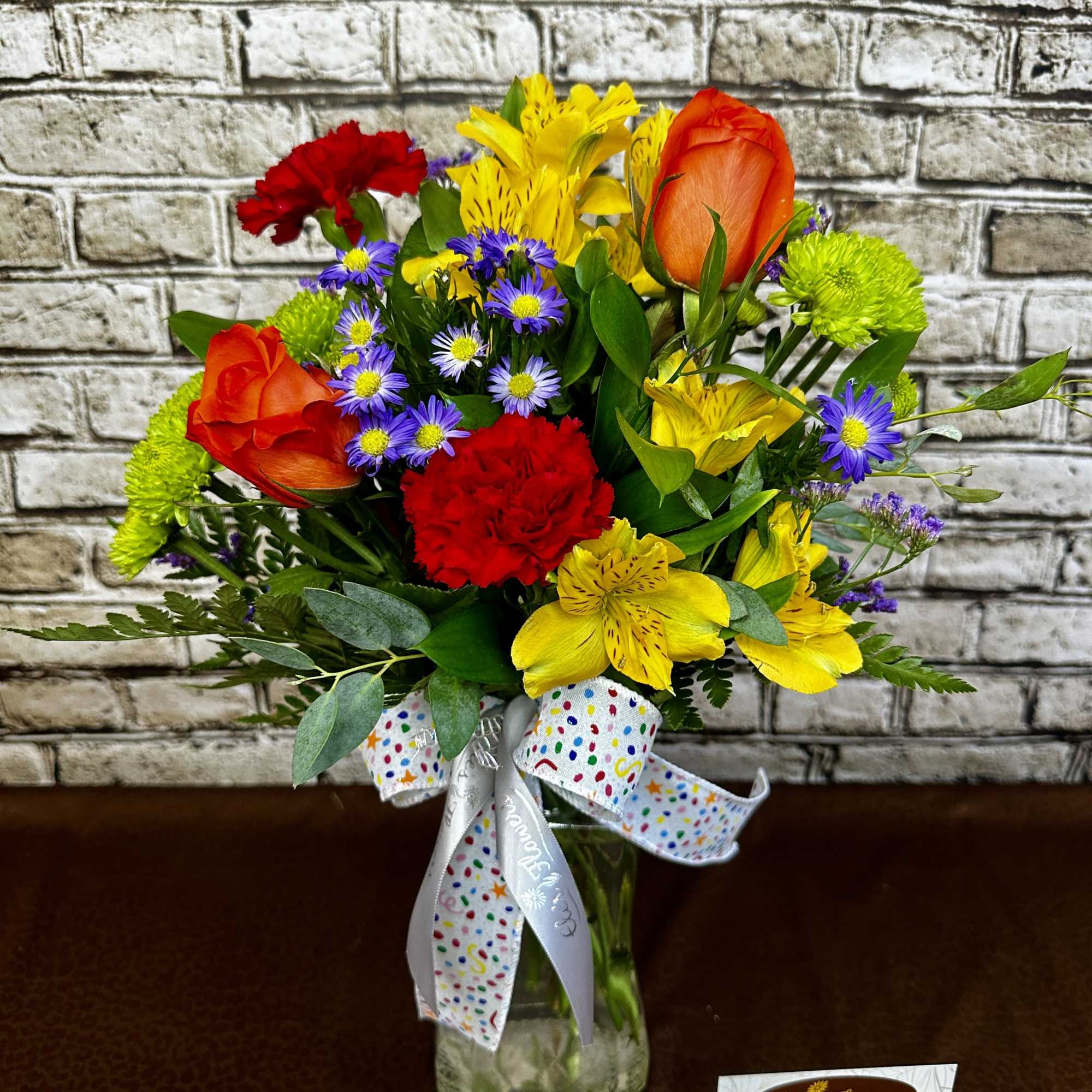 Colorful bouquet of mixed flowers in a glass vase with a polka-dot ribbon