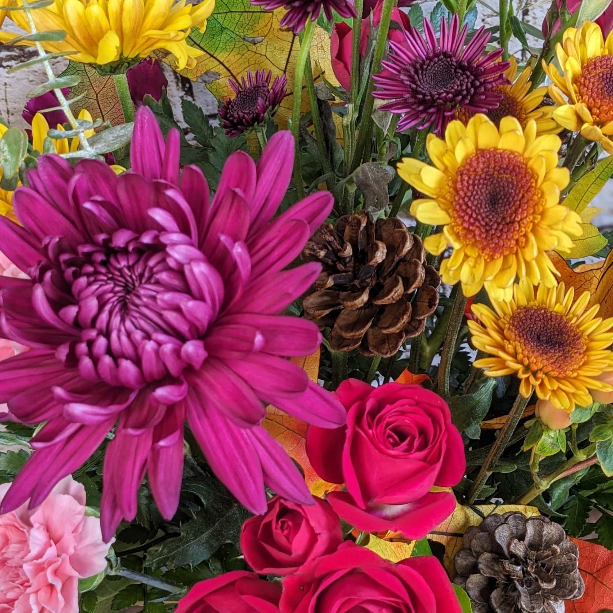Bright mixed bouquet with pink roses, yellow and purple daisies, and pinecones