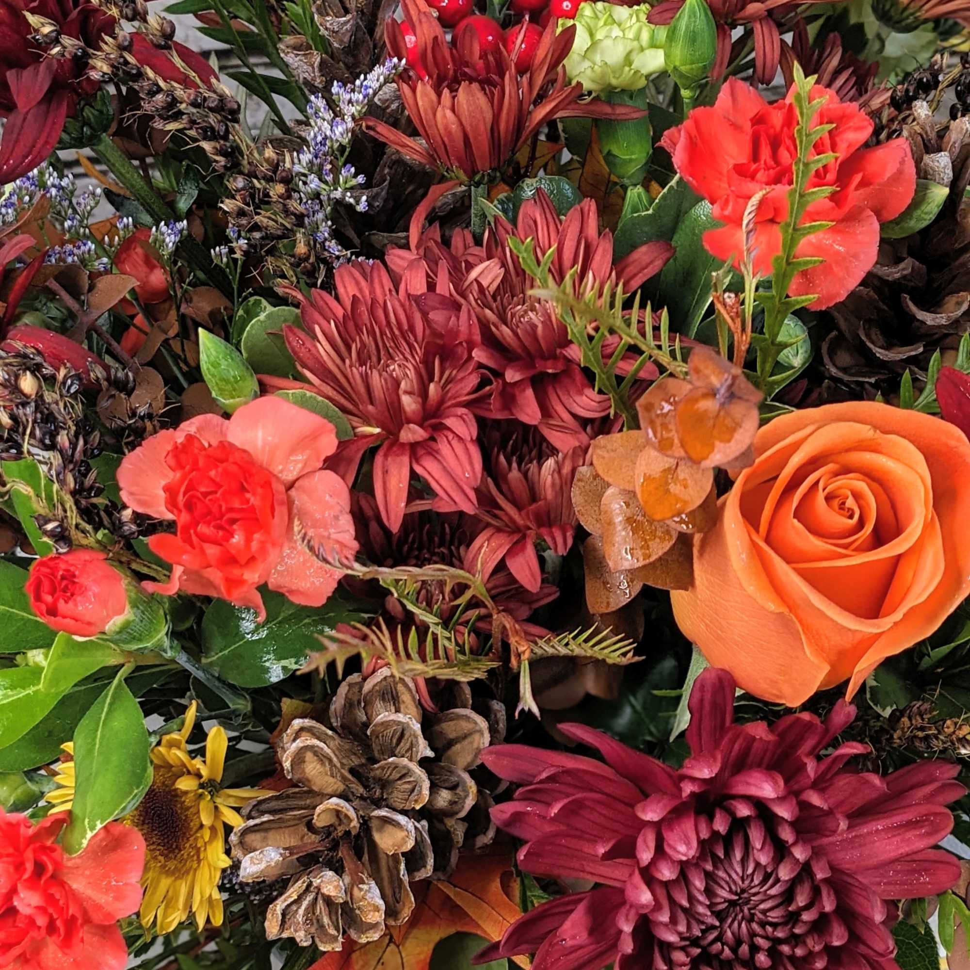 Bouquet of orange and burgundy flowers with pinecones and berries