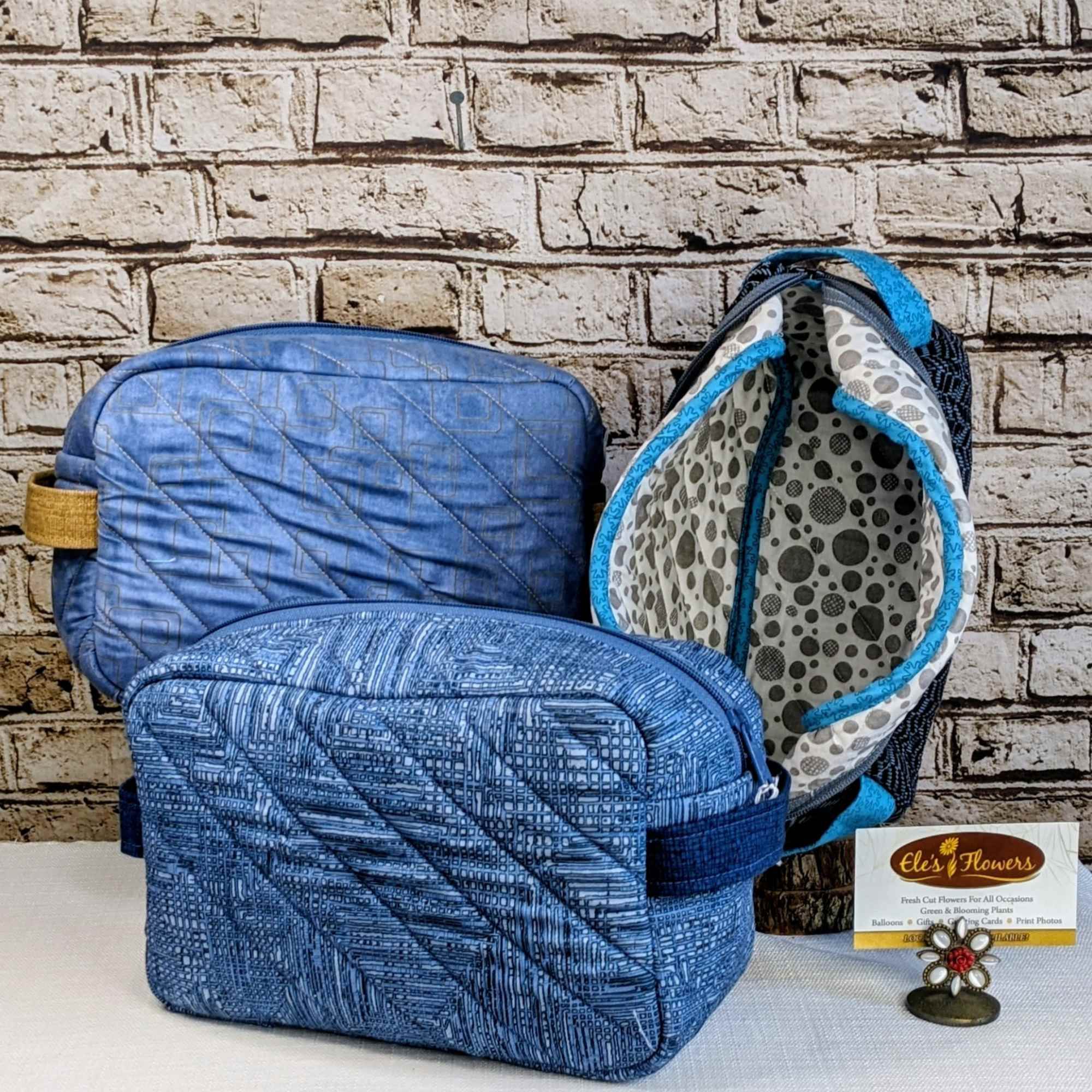 Three blue quilted zip pouches on a table with a small flower-shaped stand
