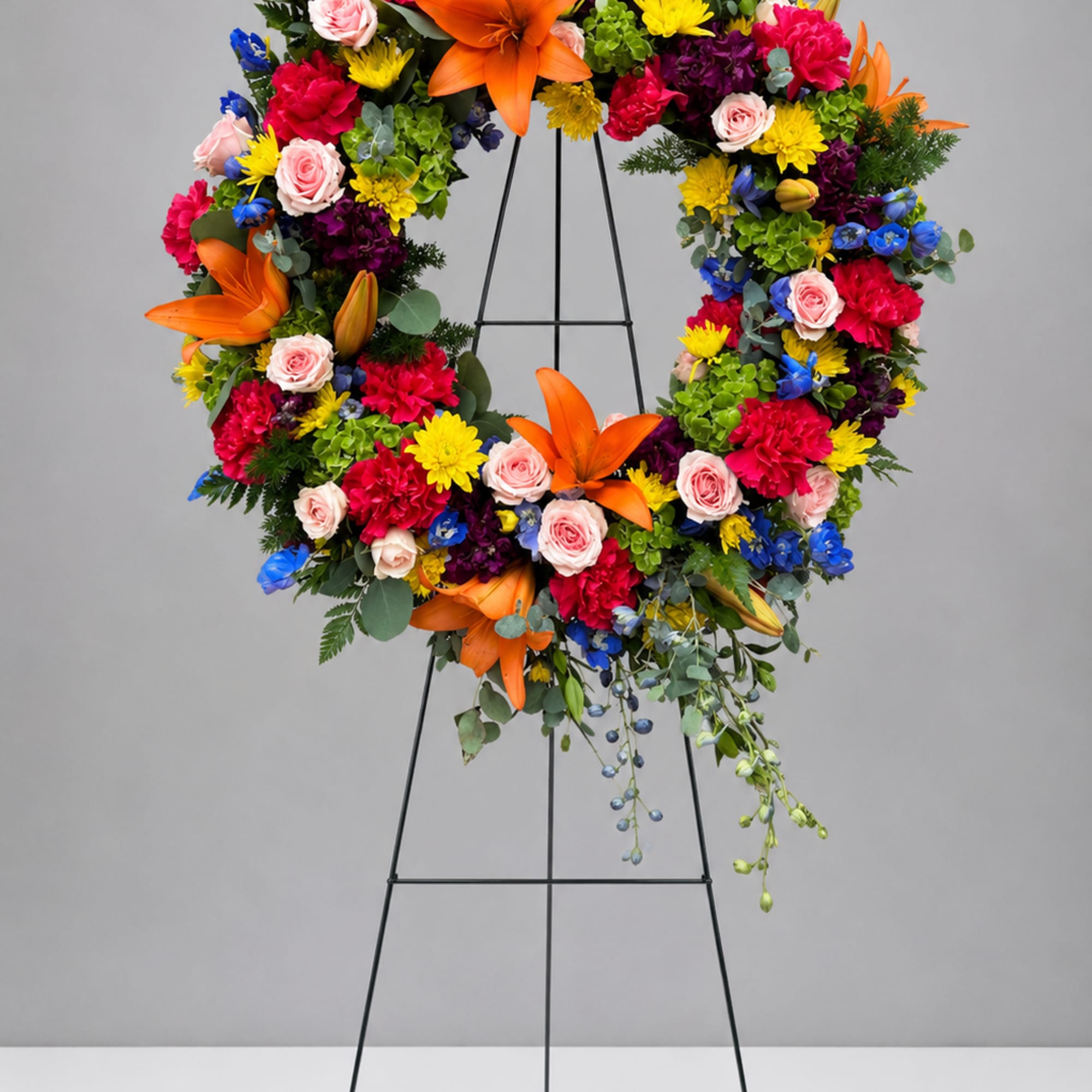 Colorful floral wreath on a black stand with orange lilies and pink roses