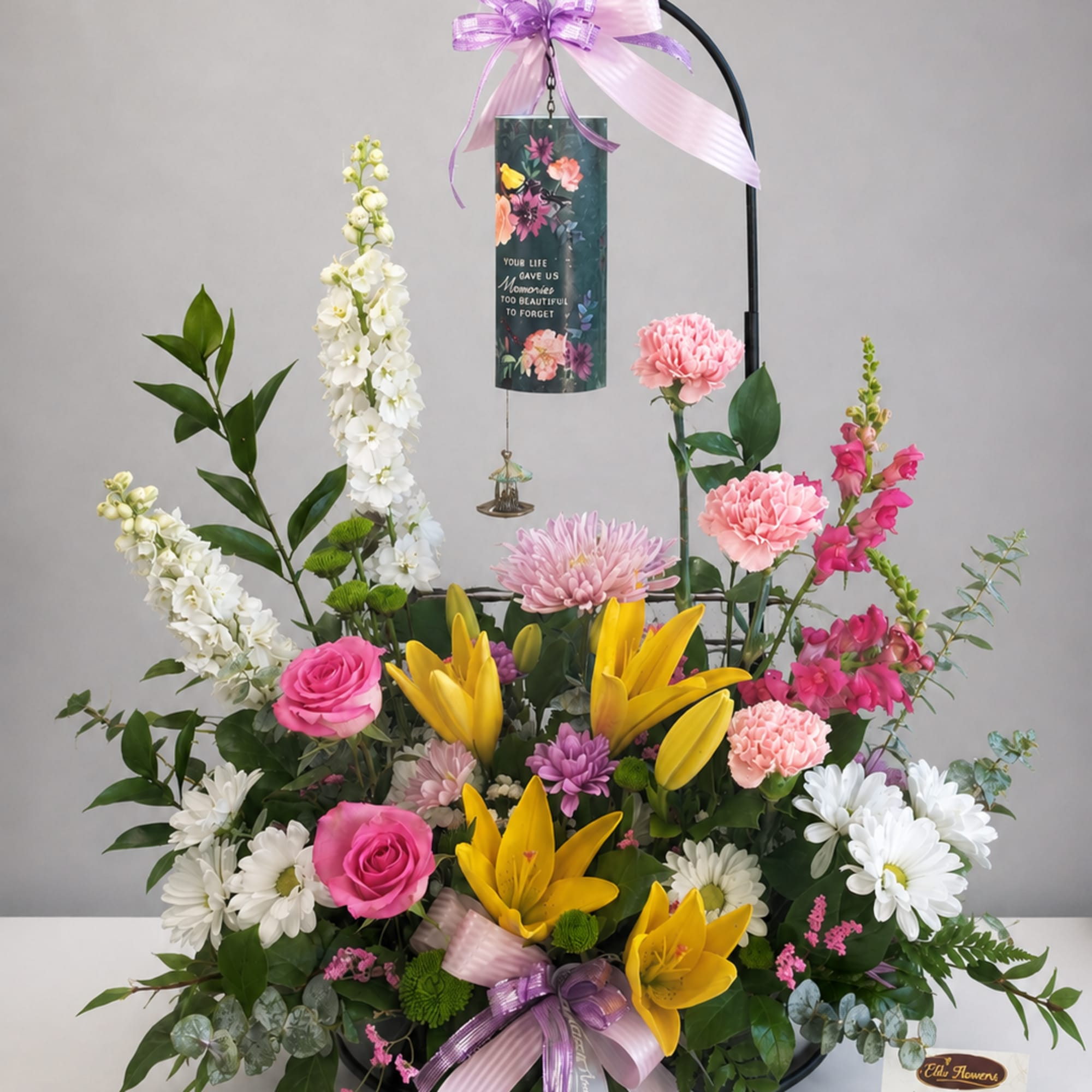 Standing floral tribute with lilies, roses, daisies, and a memorial plaque