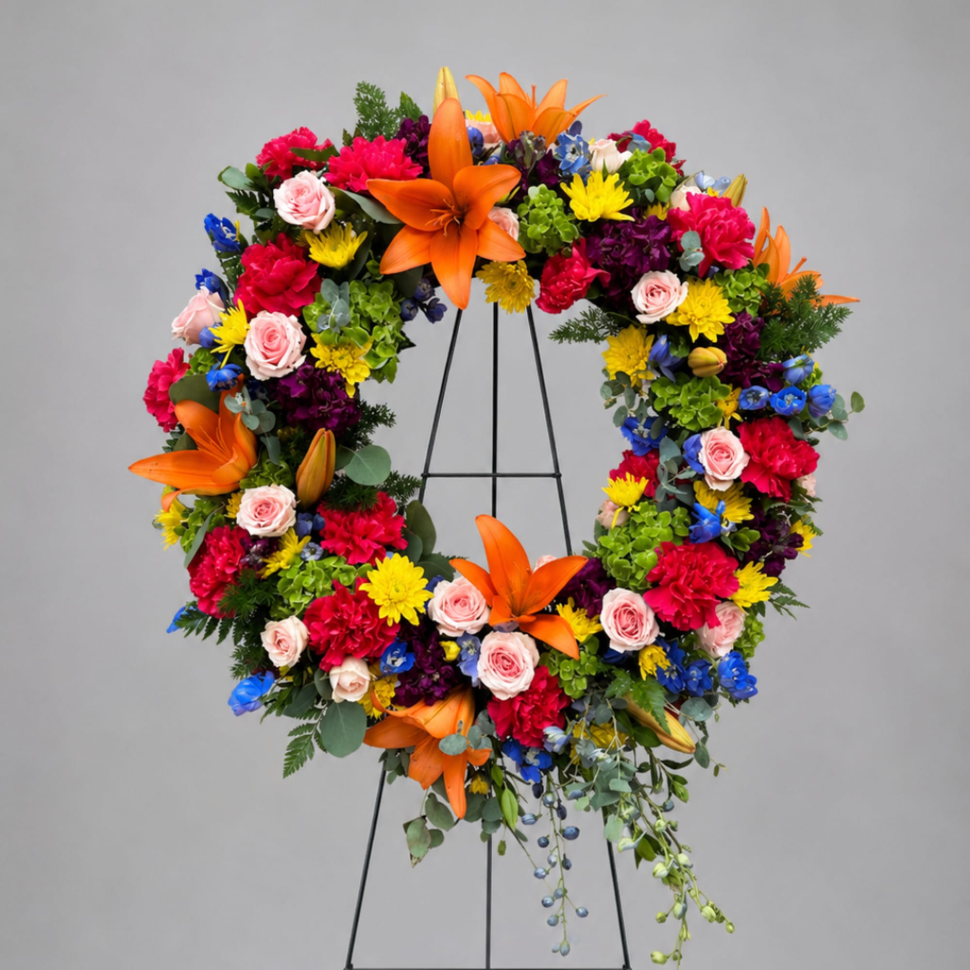 Colorful floral wreath on a black stand with orange lilies and mixed blooms