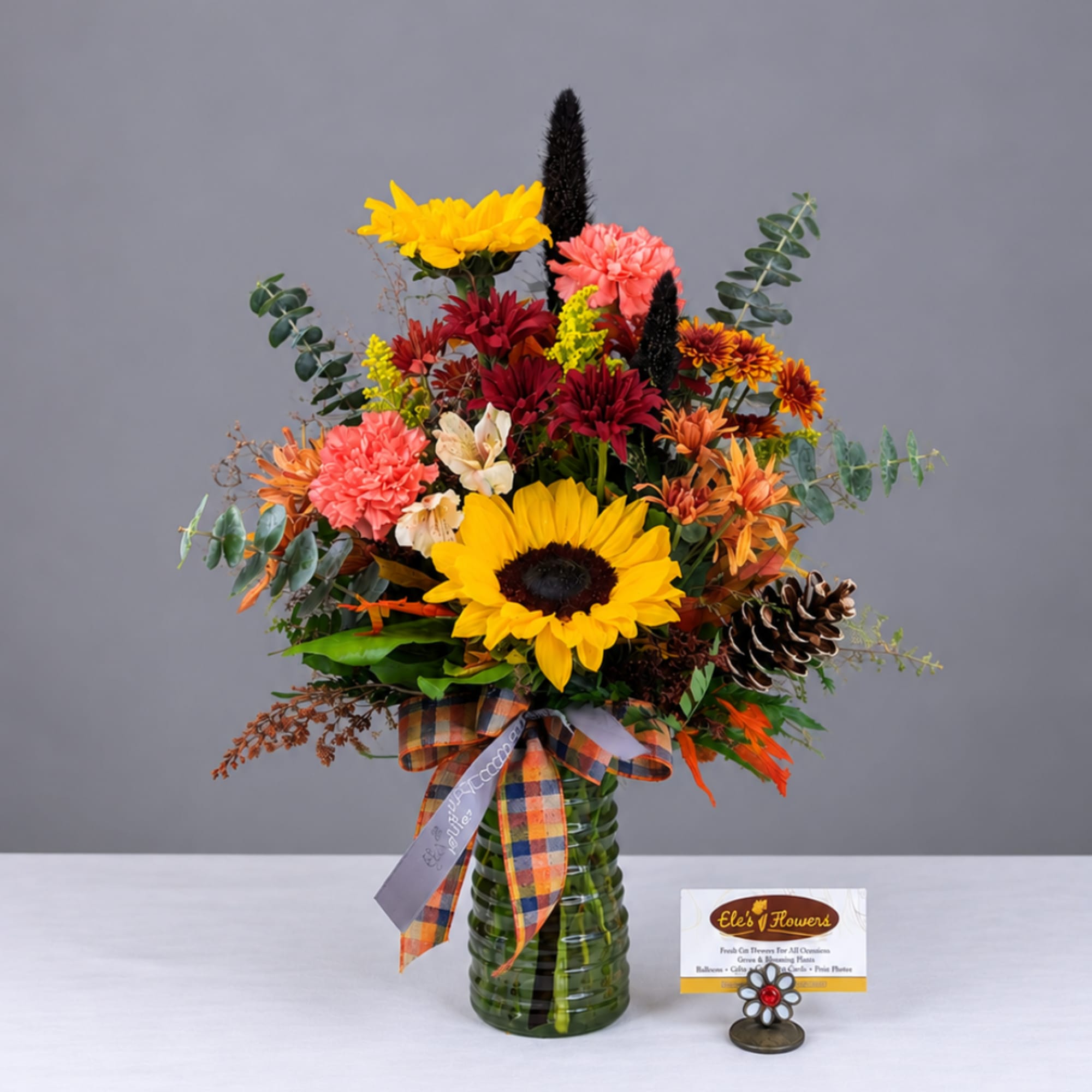 Mixed autumn bouquet in a green glass vase with a plaid ribbon