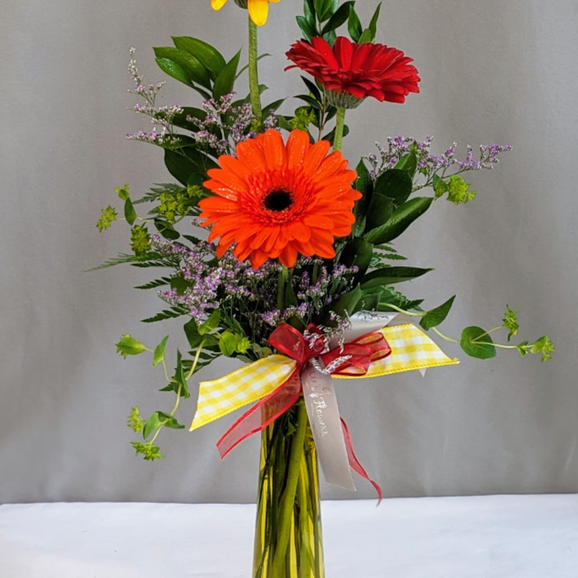 Gerbera daisy arrangement in a tall yellow vase with a ribbon bow