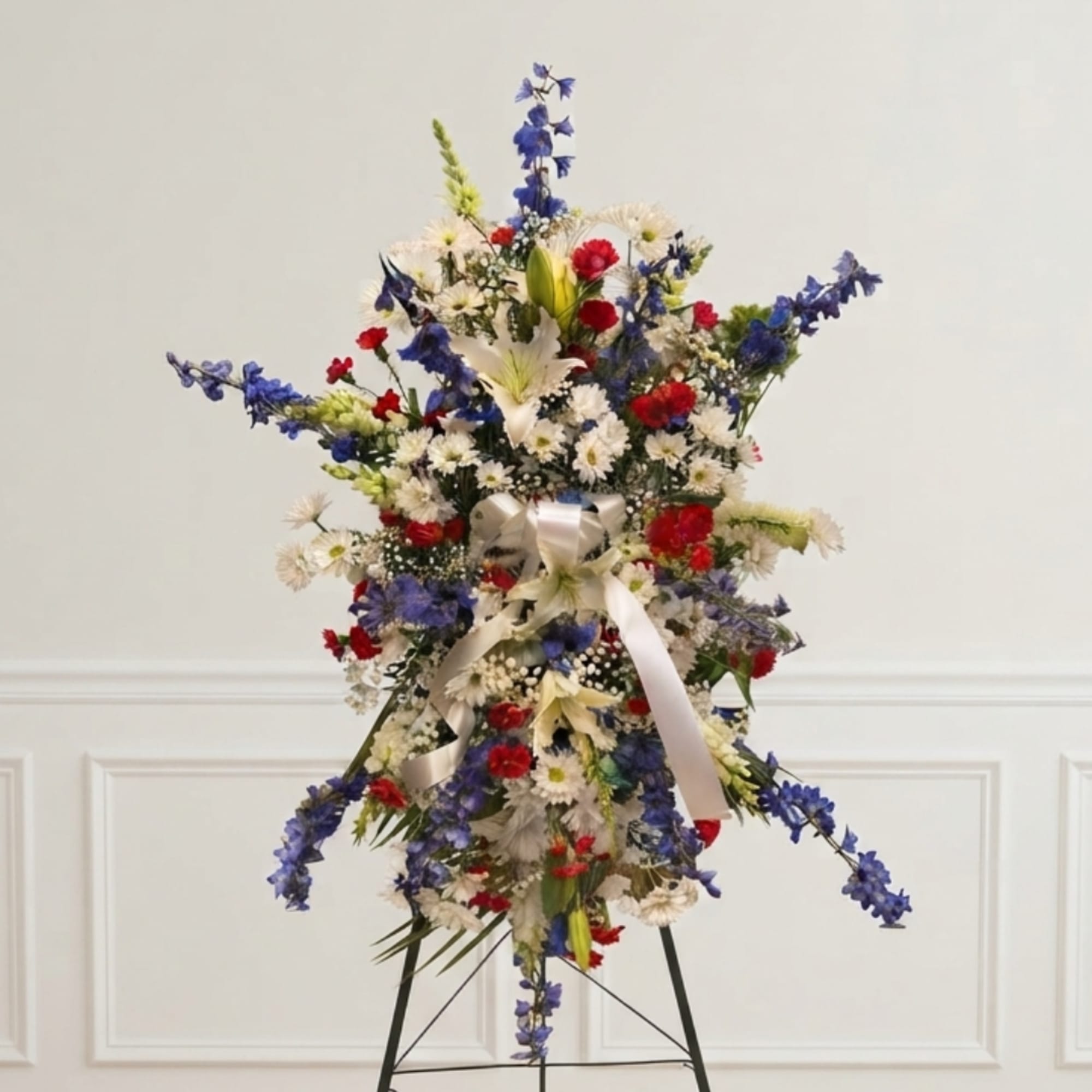 Tall floral standing spray with blue, white, and red flowers on an easel
