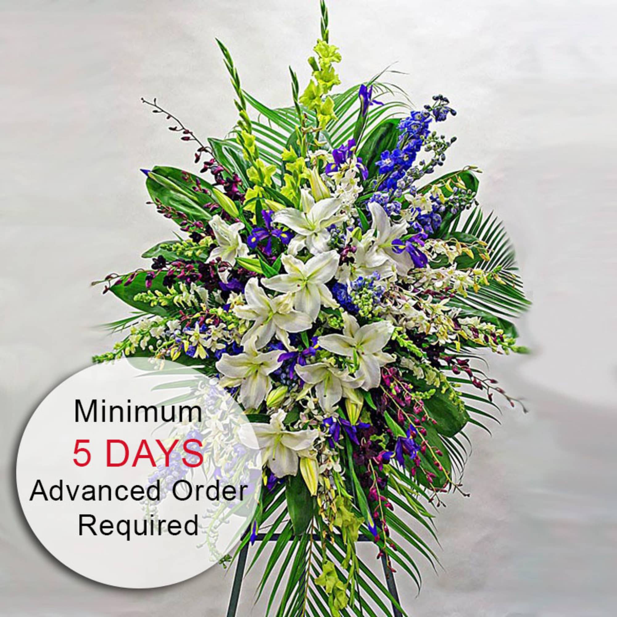 Tall standing spray of white lilies with purple and yellow flowers on a green leaf backdrop