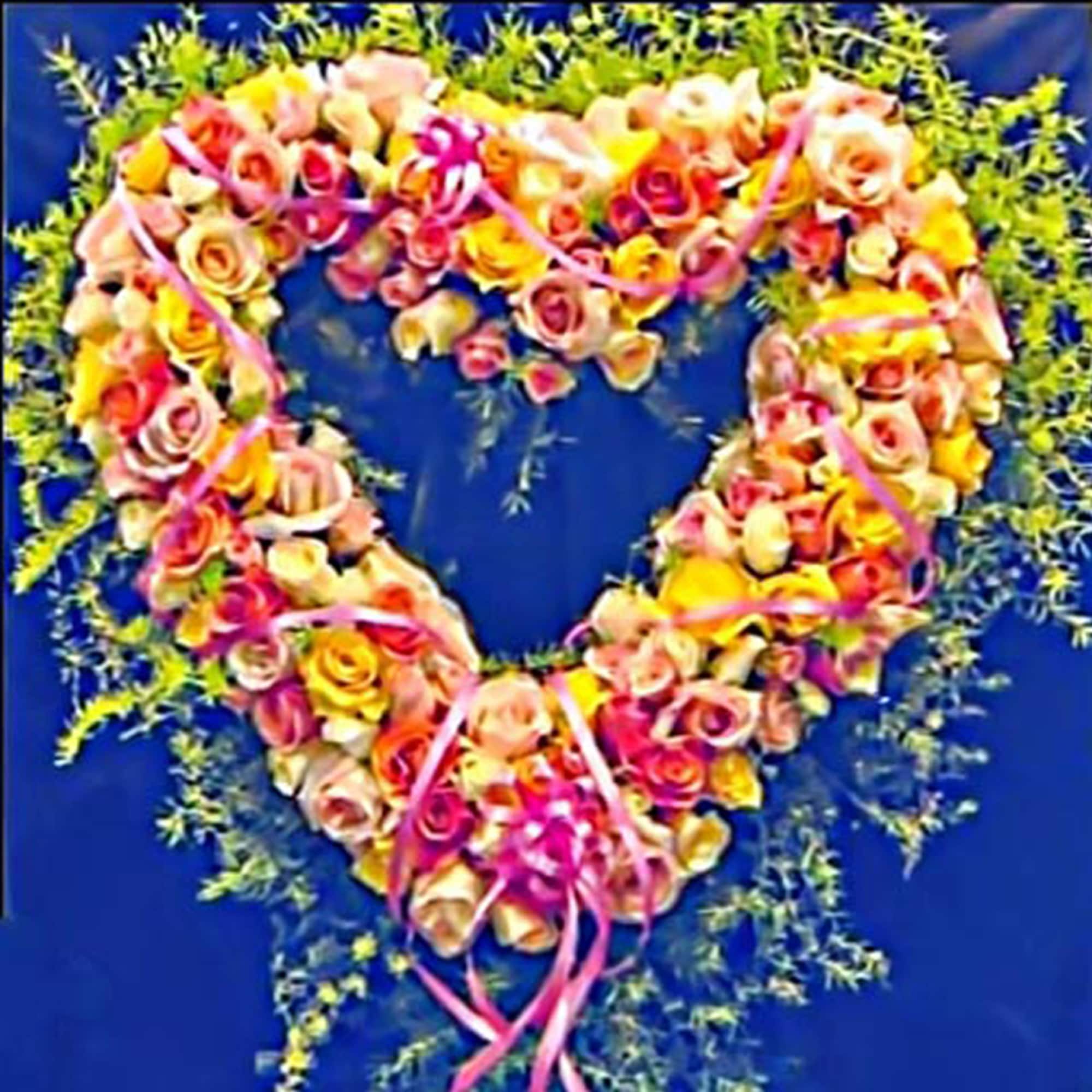 Heart-shaped wreath of pink, peach, and yellow roses with ribbons on a dark background
