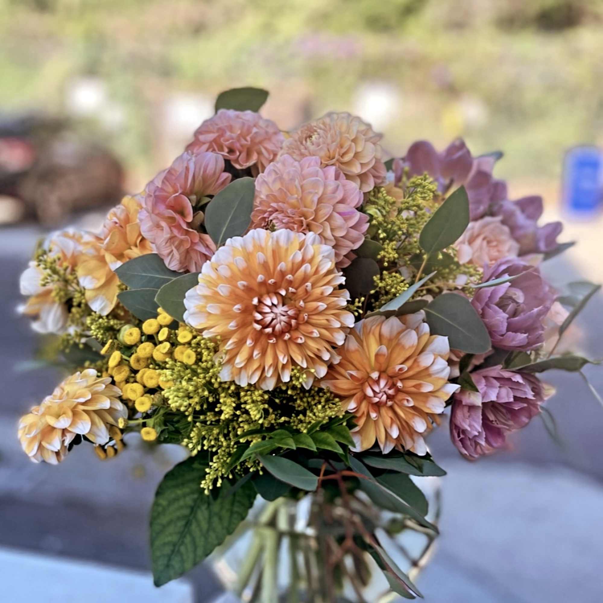 Peach and yellow dahlia bouquet with yellow filler flowers in a clear glass vase