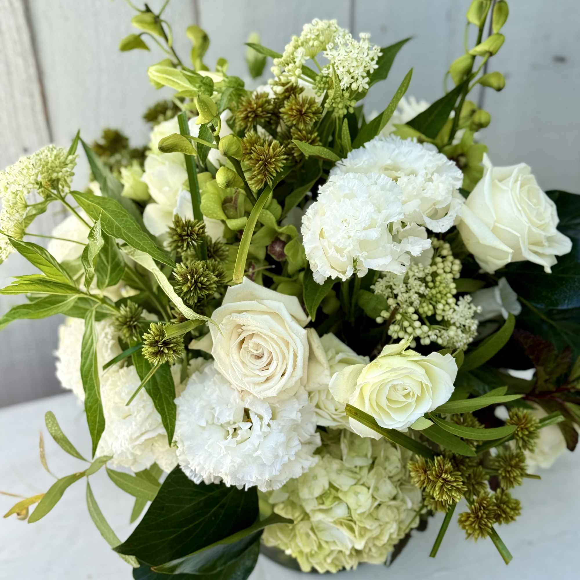 White roses and carnations arranged with green accents in a bouquet
