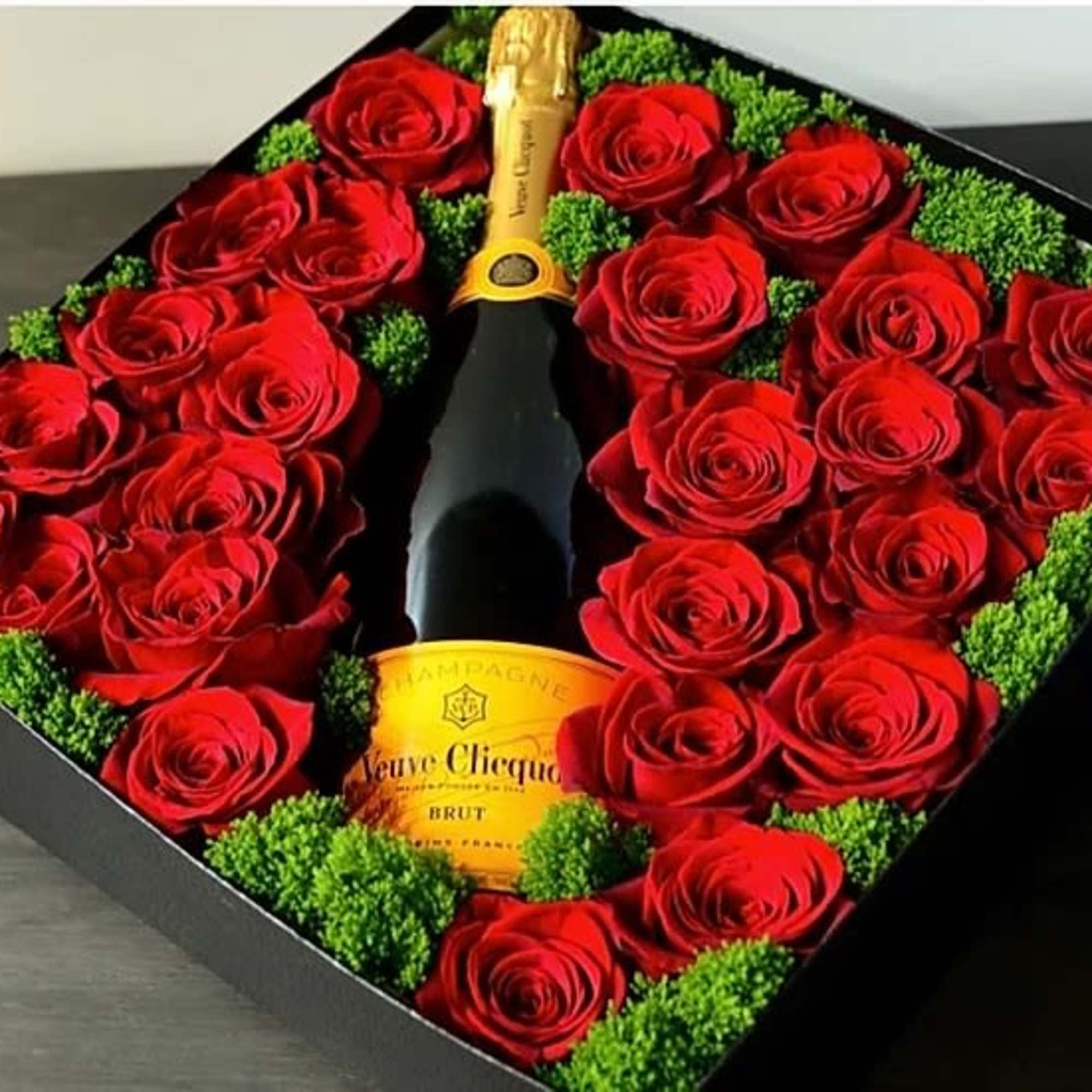 Red roses arranged around a champagne bottle in a black gift box