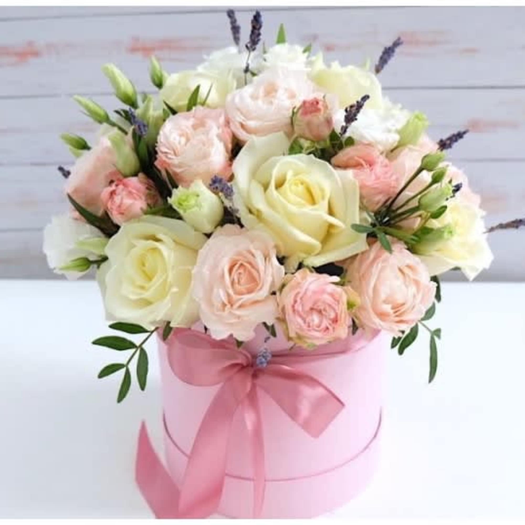 Pink and cream roses arranged in a pink hat box with a ribbon