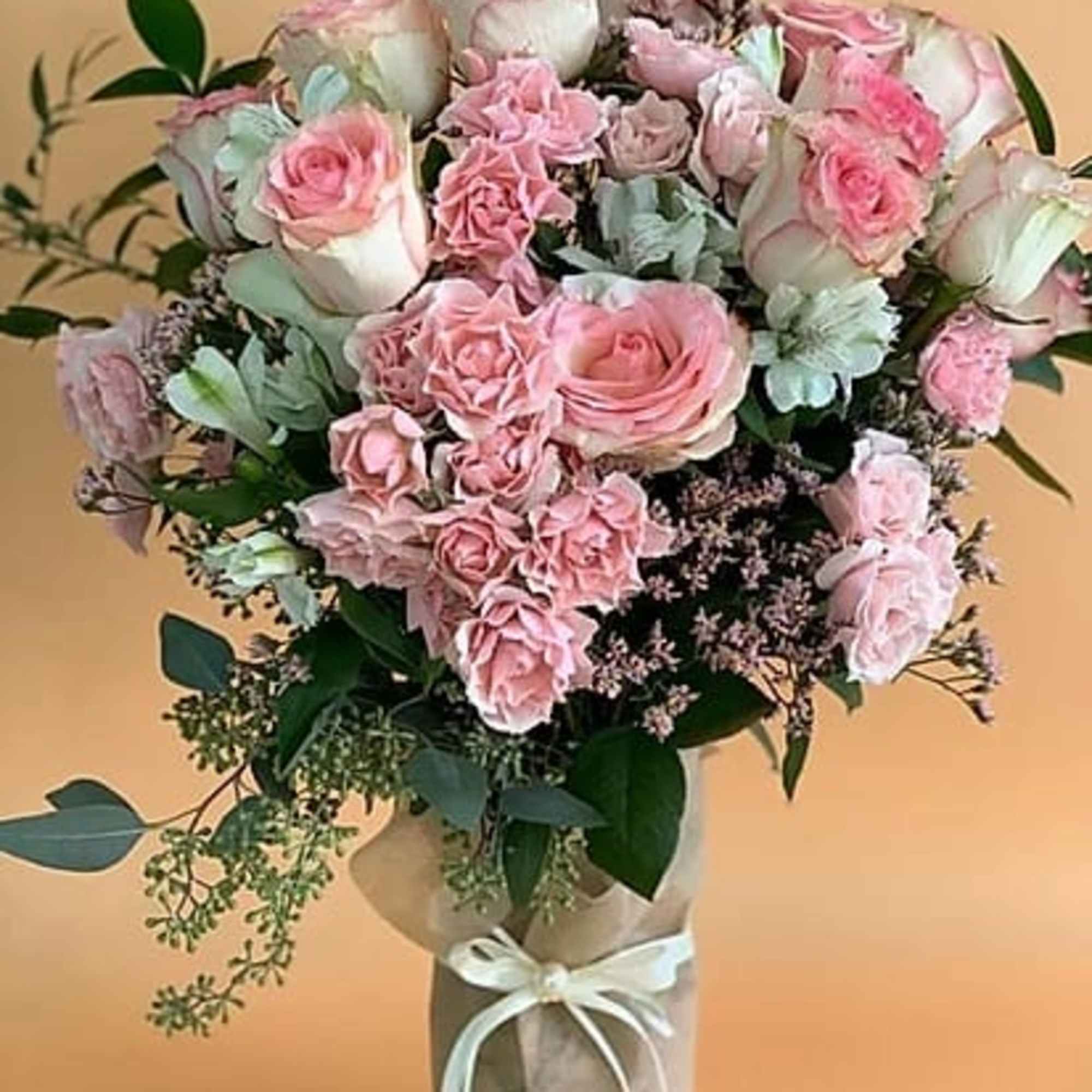 Pink roses and carnations arranged in a wrapped vase bouquet