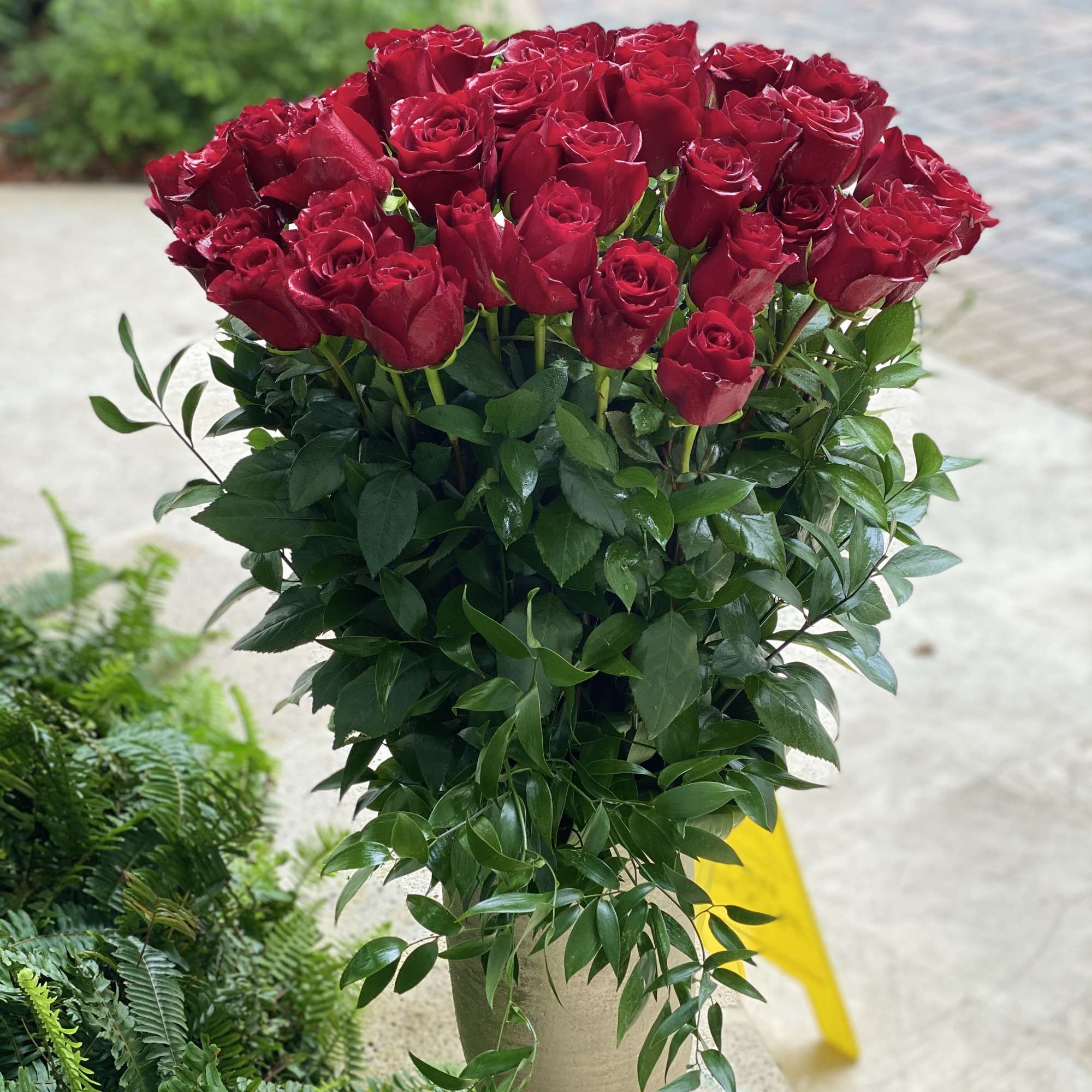 Red roses arranged in a tall beige vase with lush greenery