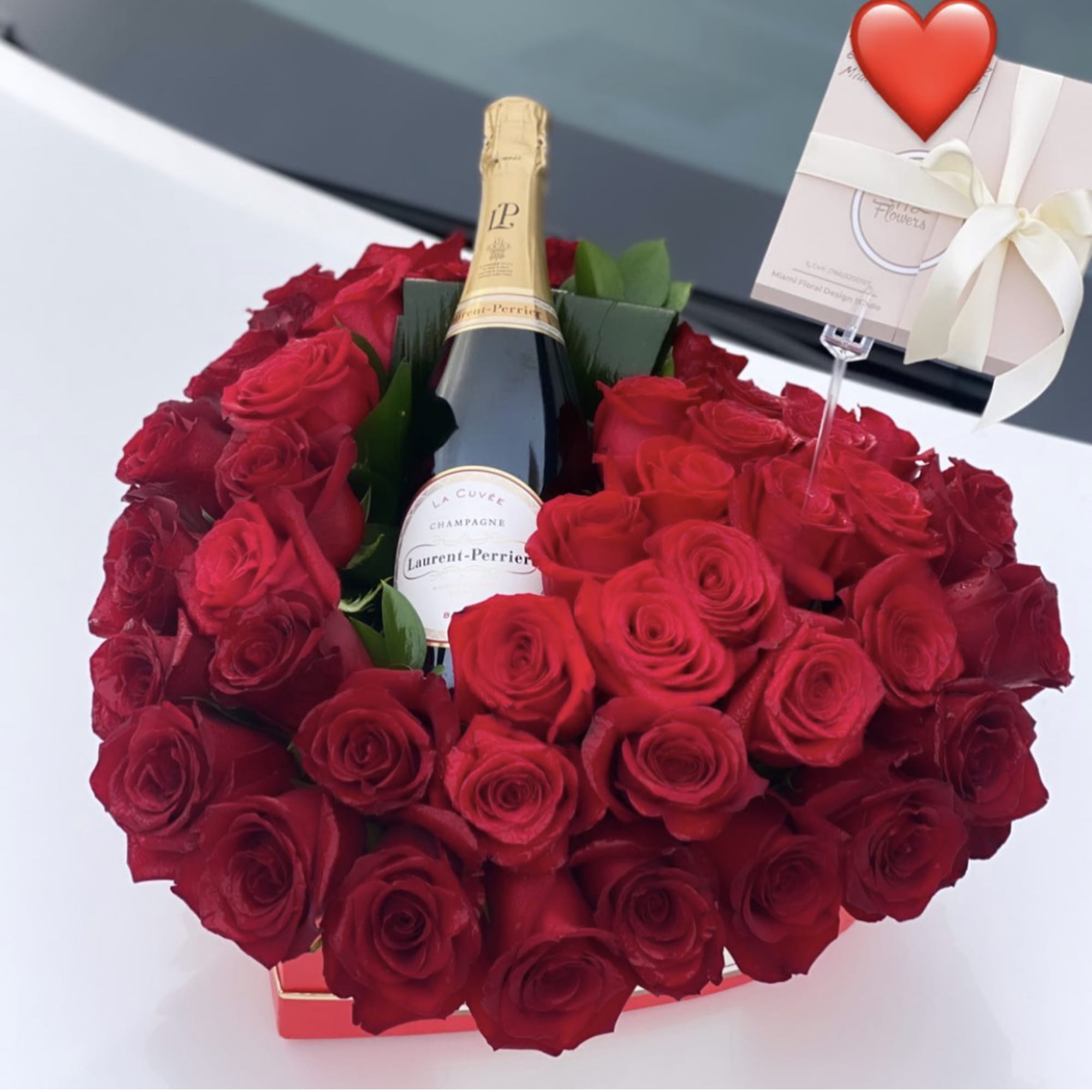 Heart-shaped red rose arrangement with a champagne bottle and gift card