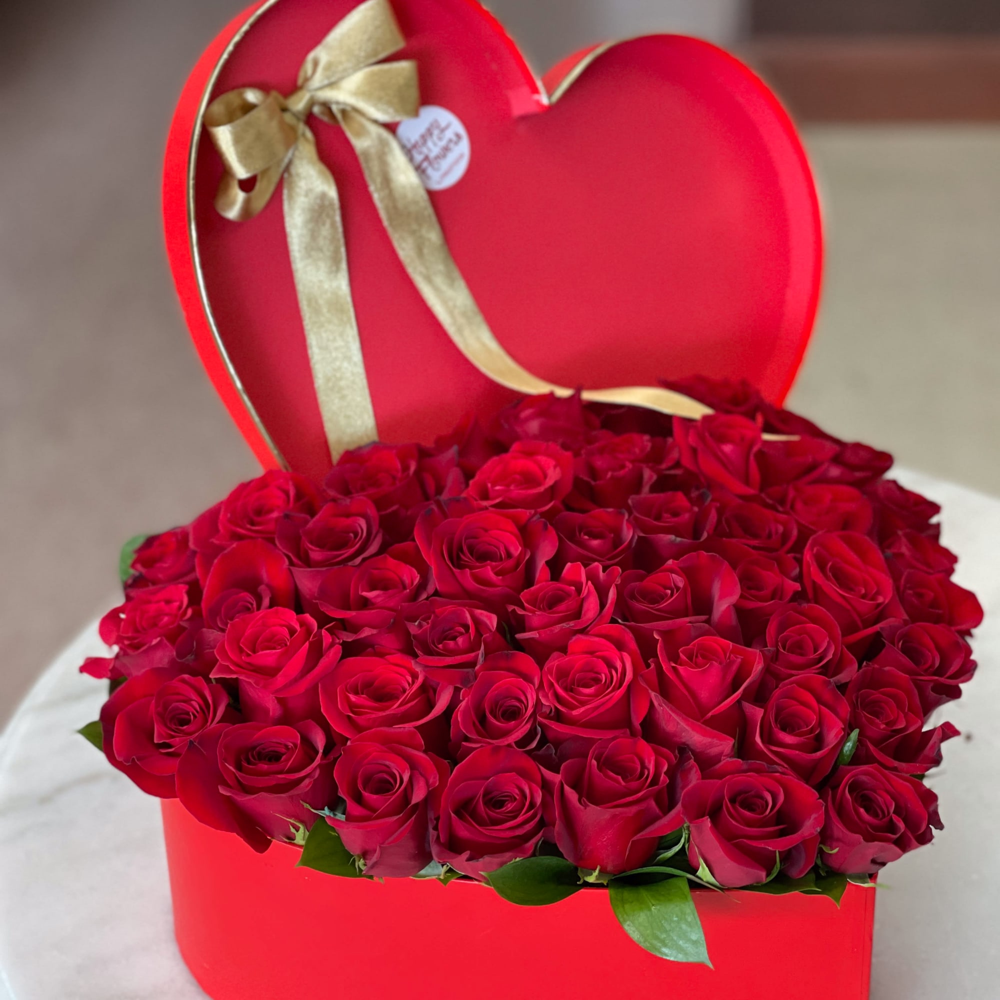 Heart-shaped box filled with red roses and a gold ribbon bow